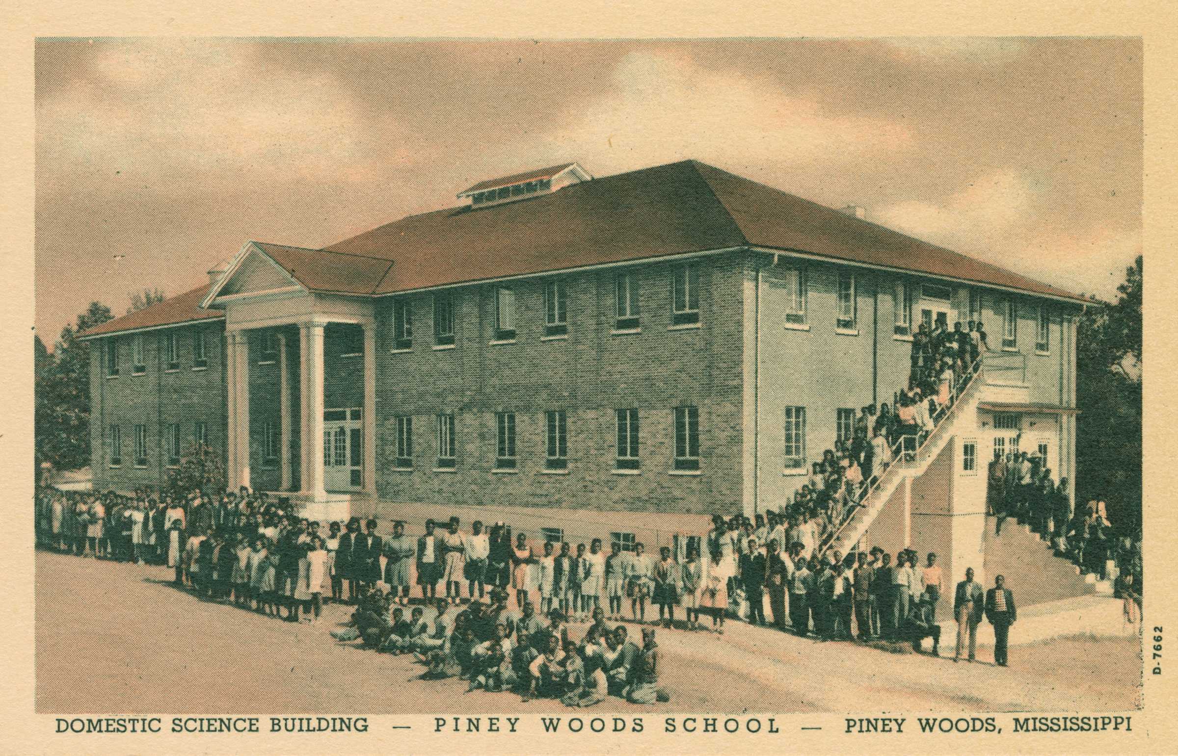 Colored postcard showing a large two story brick building with school children lined up in from and to the side of it.  The post card identifies the school as "DOMESTIC SCIENCE BUILDING - PINEY WOODS SCHOOL - PINEY WOODS, MISSISSIPPI."