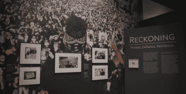 Corner of the gallery with an protest image cover the gallery wall. The art and title of the exhibit featured.