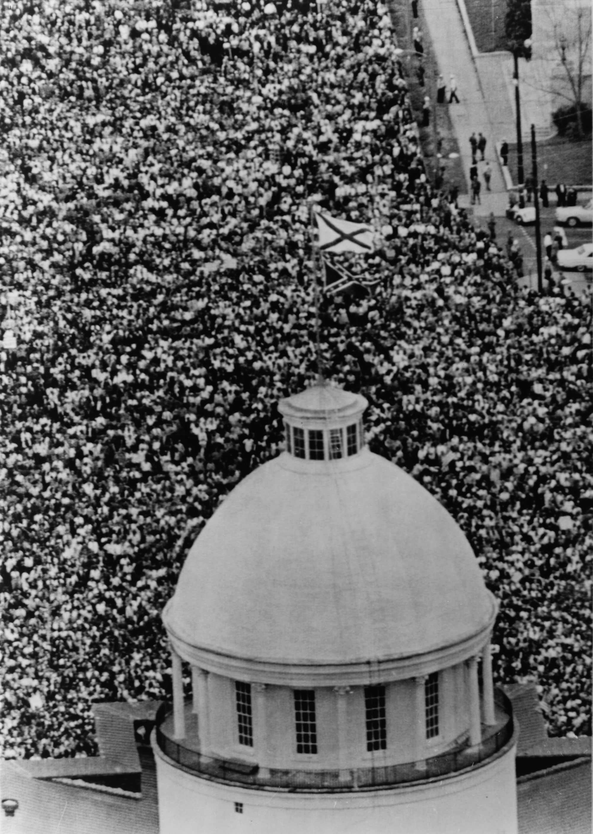 A black and white photograph of an aerial view of a large crowd of demonstrators gathered outside the Alabama state capitol.