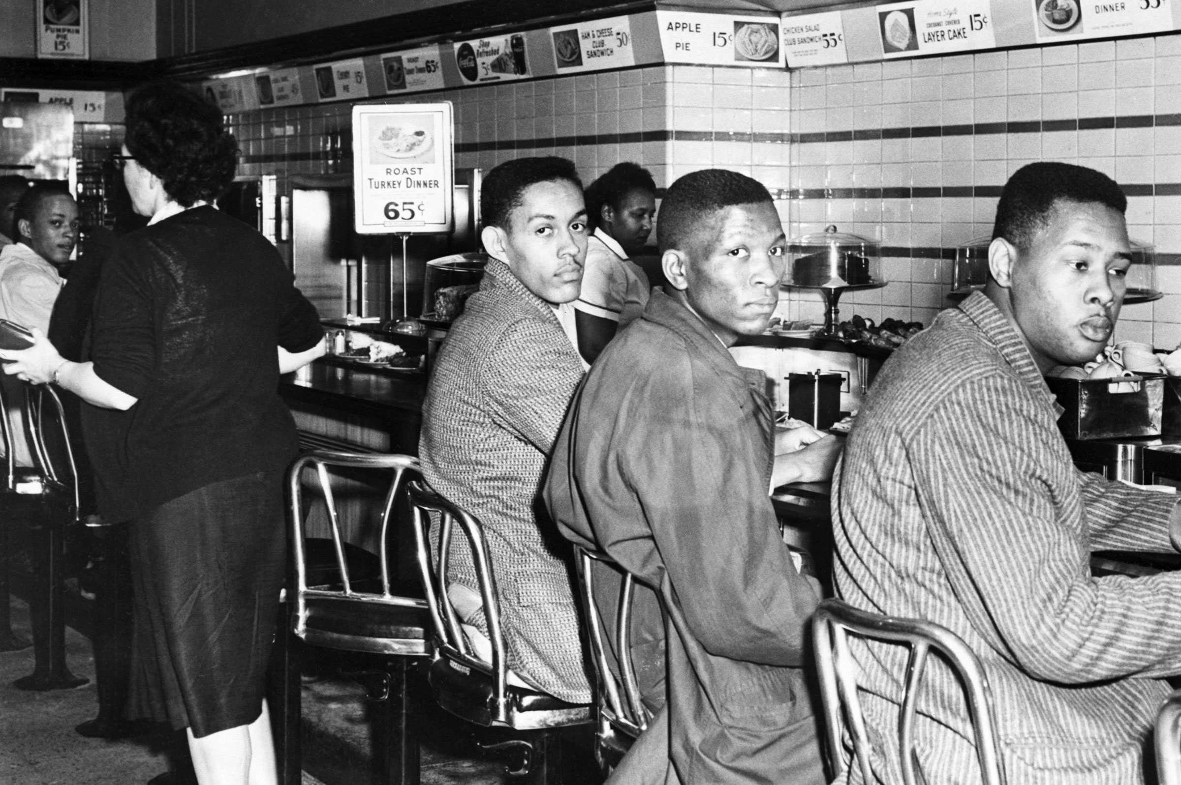 North Carolina A&T college students sit at Woolworth’s counter. The men are dressed nicely, looking at the camera with sterns look.