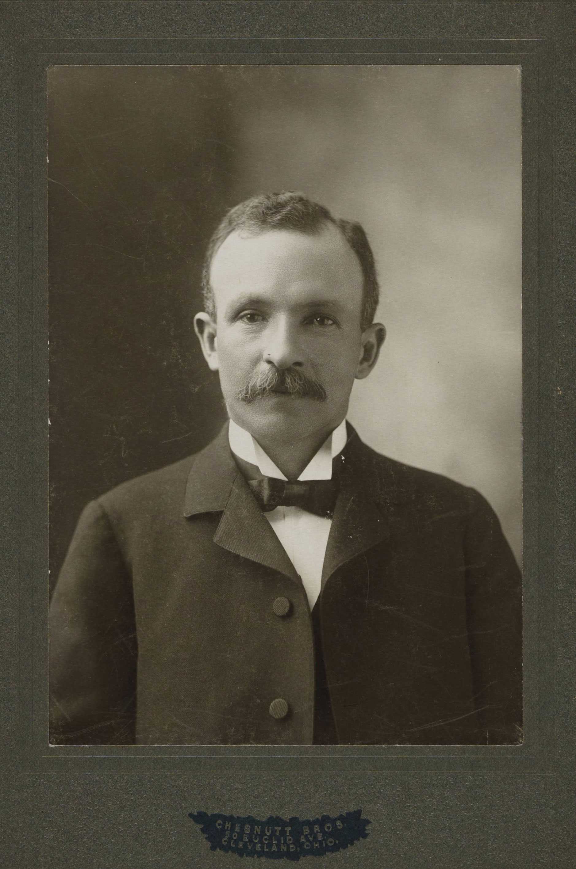 Photographic portrait of a man with a mustache wearing a suit coat, white shirt and bow tie.