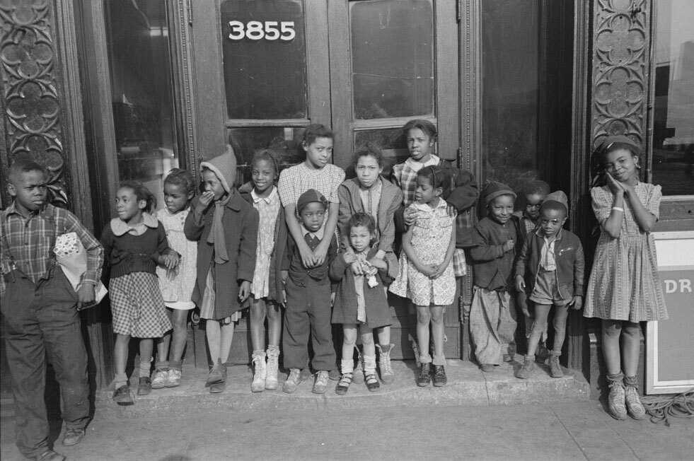 A black and white photograph of children standing together outside of a New York City building.