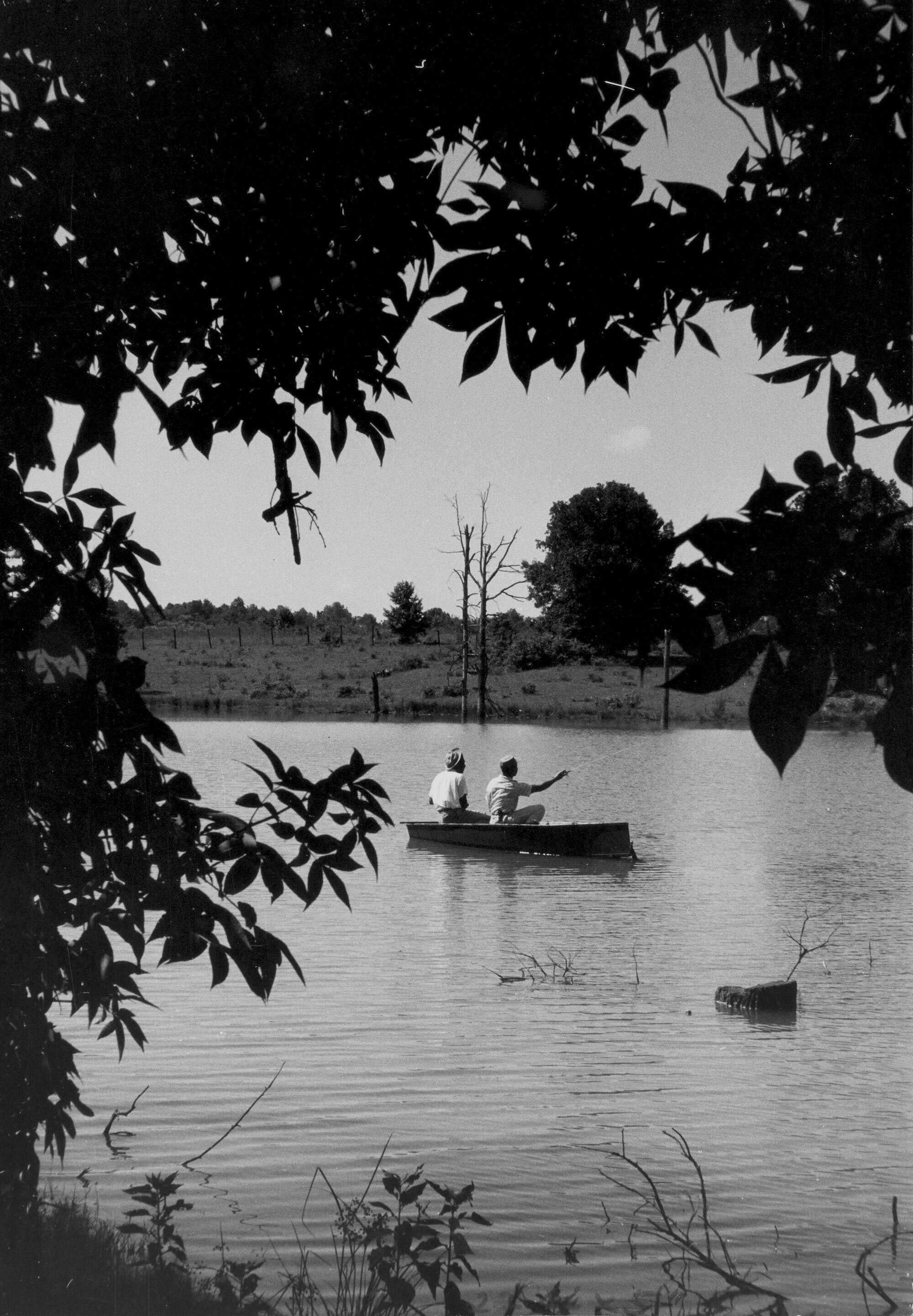 Black and white photograph of two men (one is Medgar Evers) fishing in a small boat on a river.