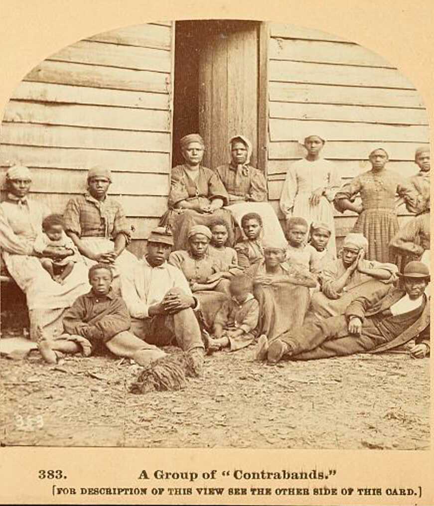 Stereograph showing a group of enslaved men, women, and children gathered outside a building