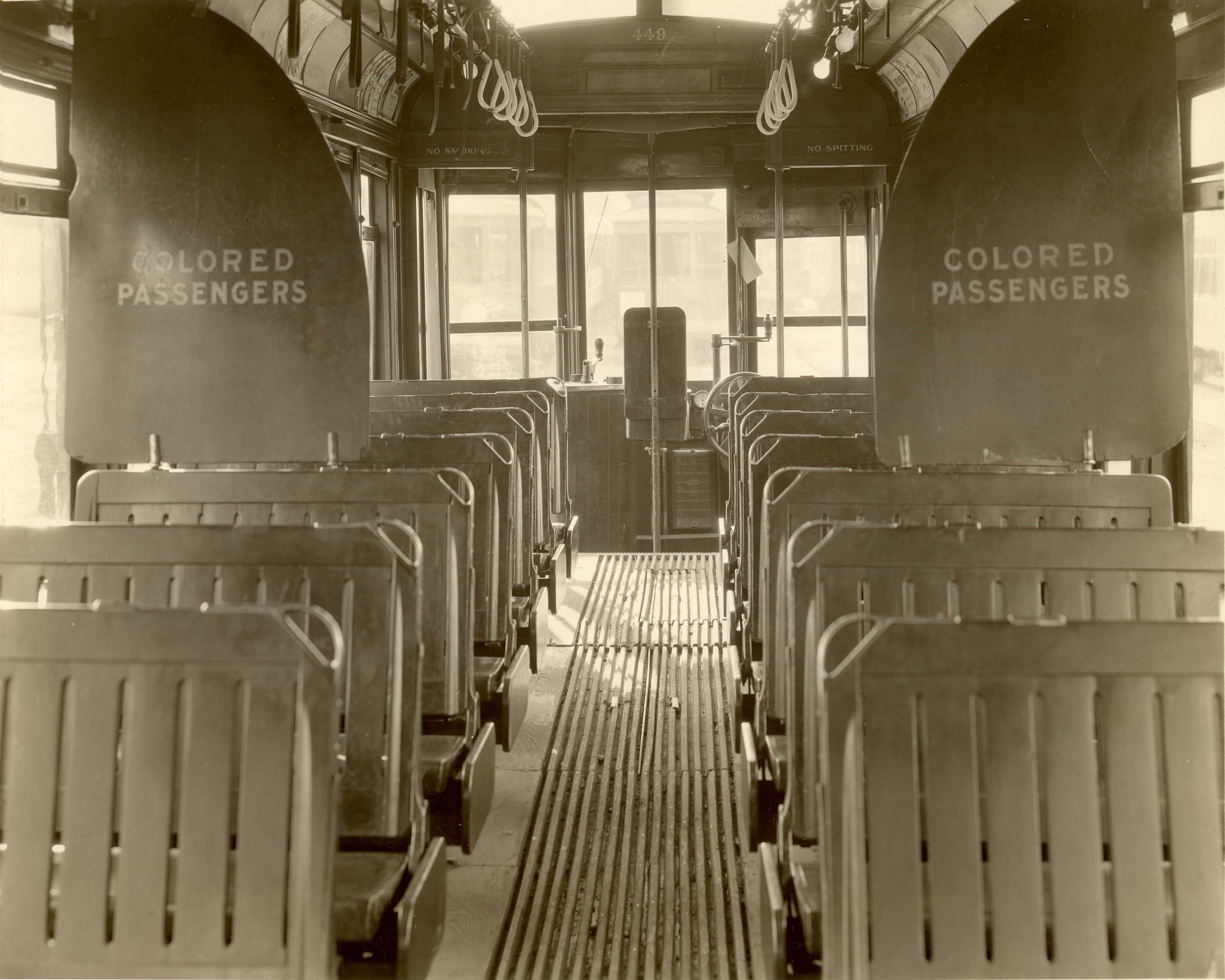 Black and white photograph of empy bus with signs "COLORED PASSENGERS" printed on partition.