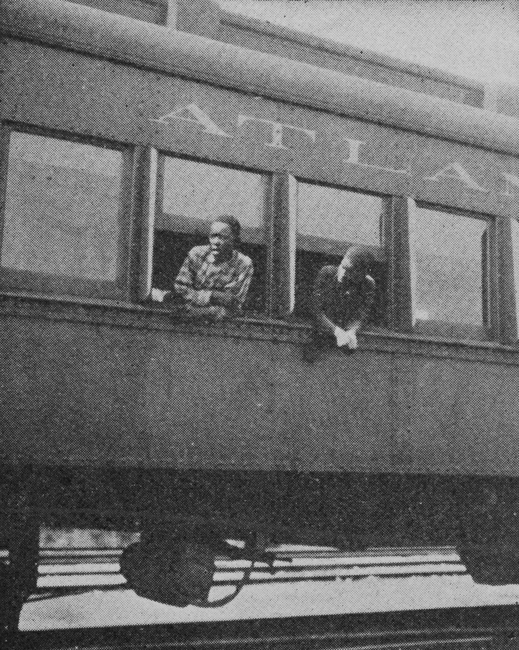 Black and white photograph of train car with two Black boys hanging out the window.