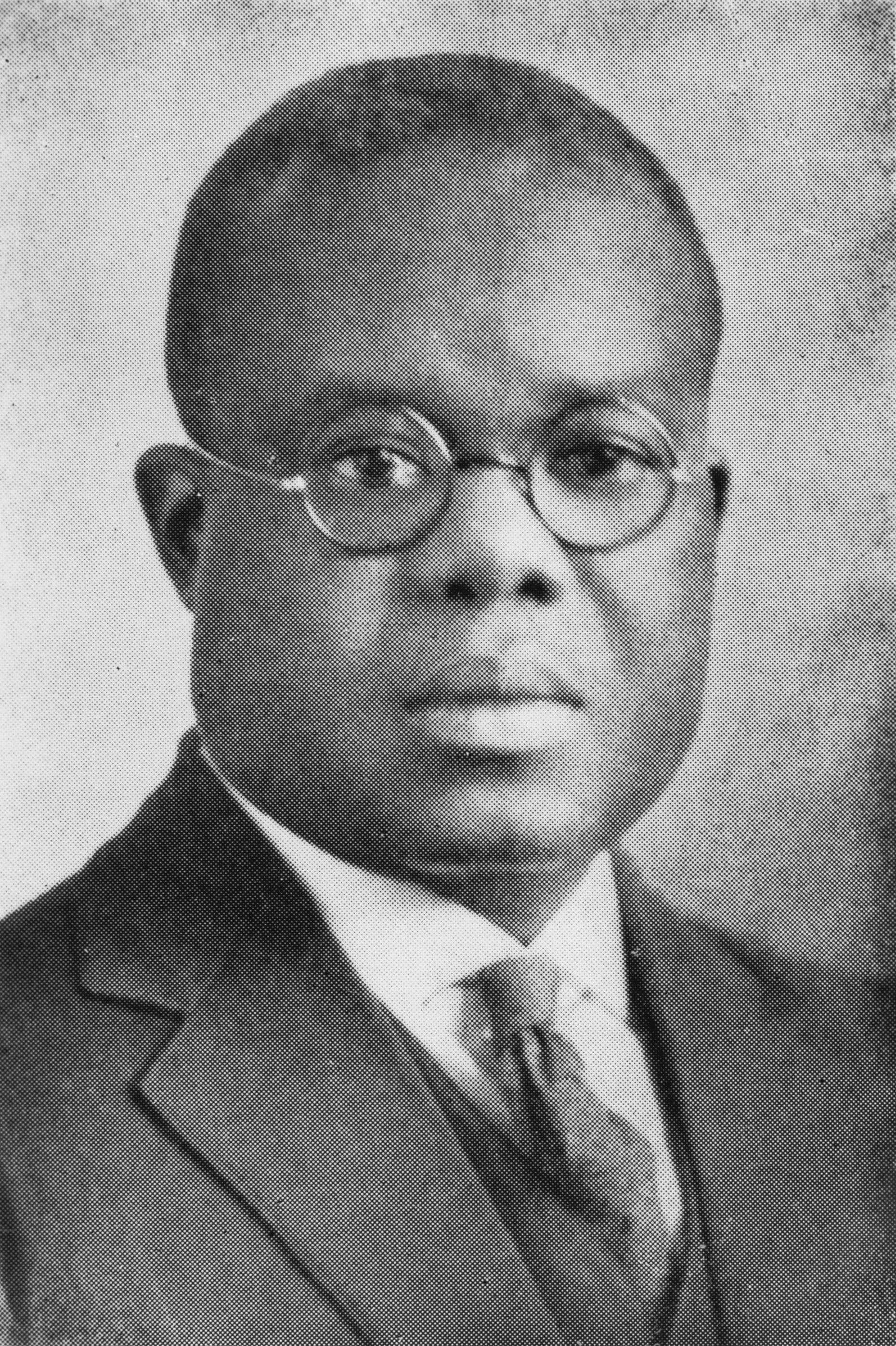 Black and white portrait of an African American man.  He is wearing round glasses and a suit.