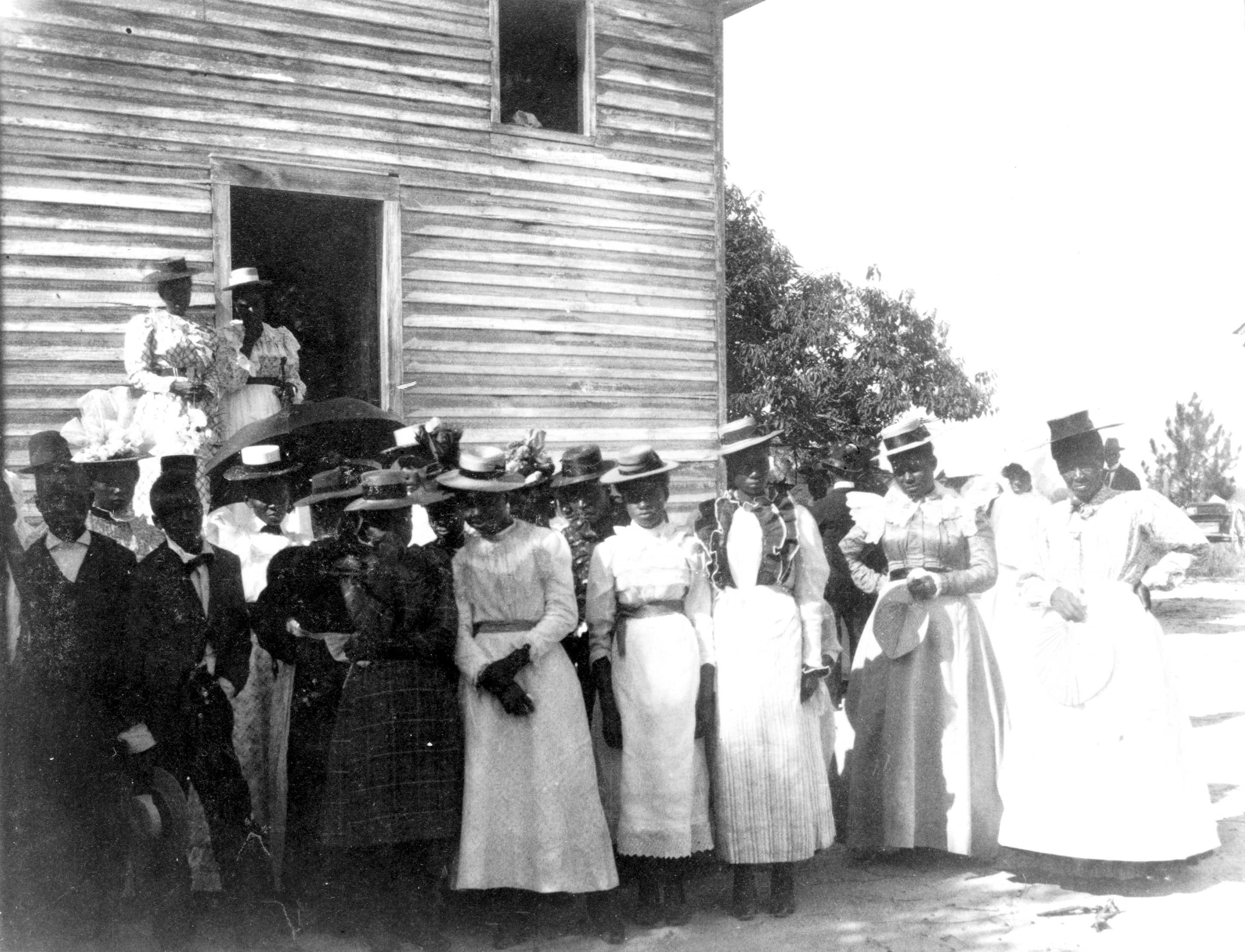 A worn black and white photograph of a group of well dressed African Americans posed outside of church.