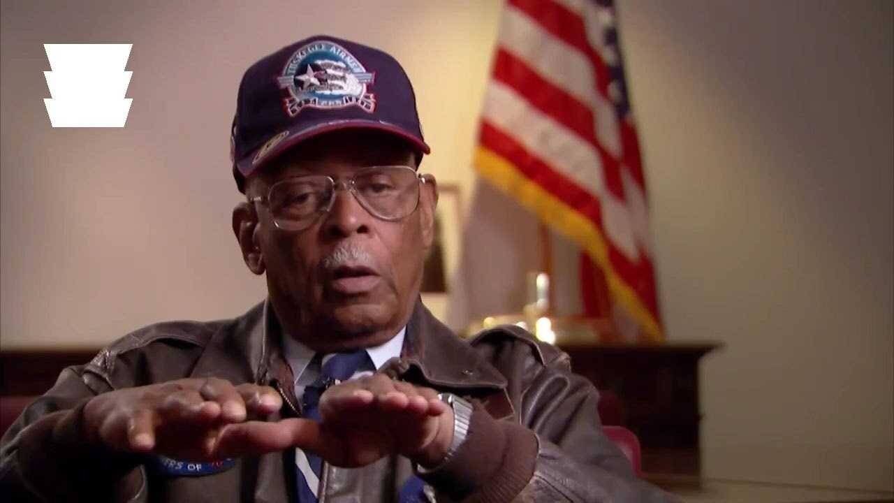 A older gentleman with airforce hat and leather jacket sitting down for an interview.