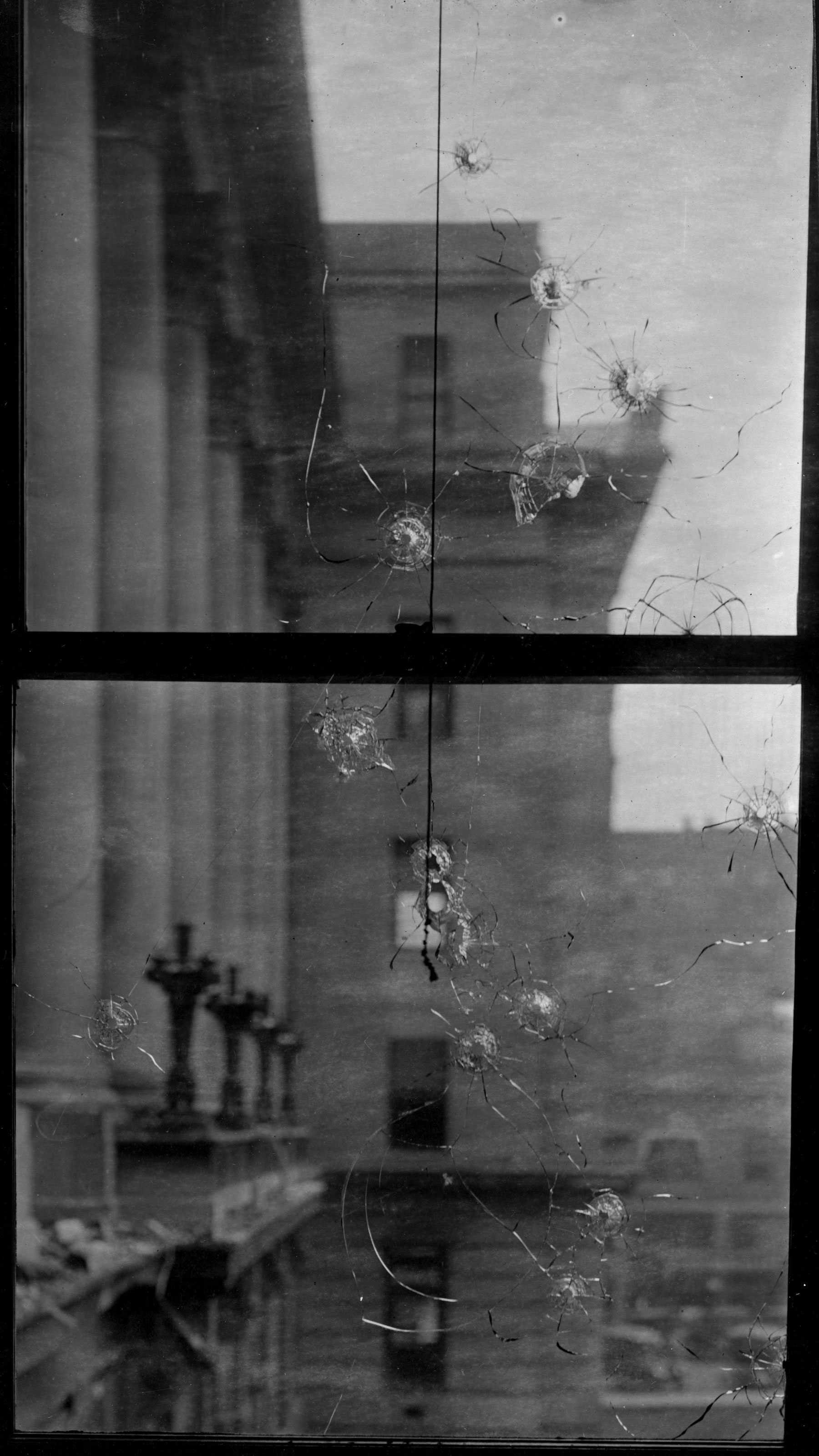 Black and white photograph of window with multiple bullet holes.