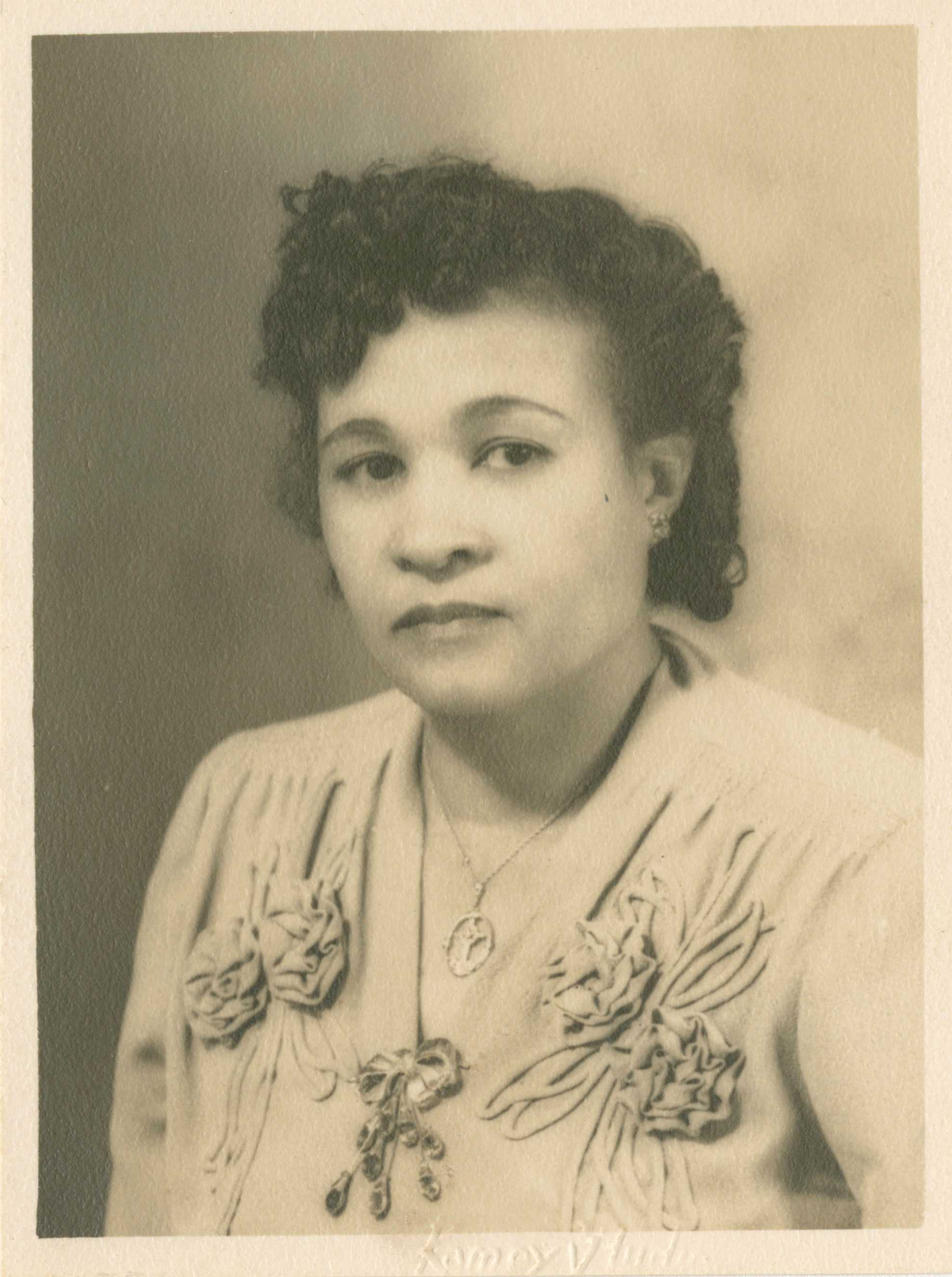 A black-and-white photograph of Frances Albrier. She faces three-quarters left wearing a dress with fabric flowers on it and a necklace.