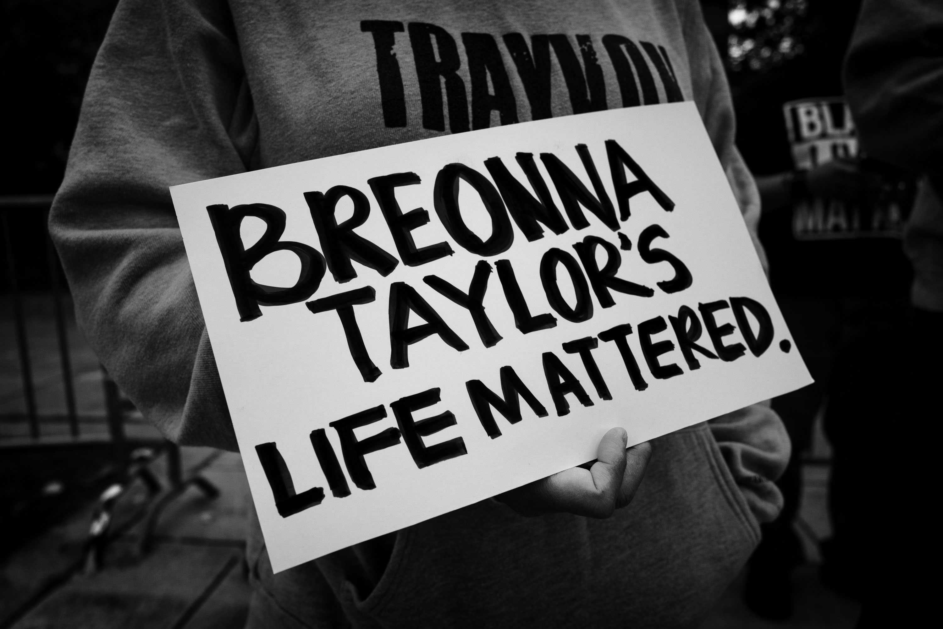 A protester holding a sign at a Black Lives Matter protest. The sign reads "BREONNA / TAYLOR’S / LIFE MATTERED."