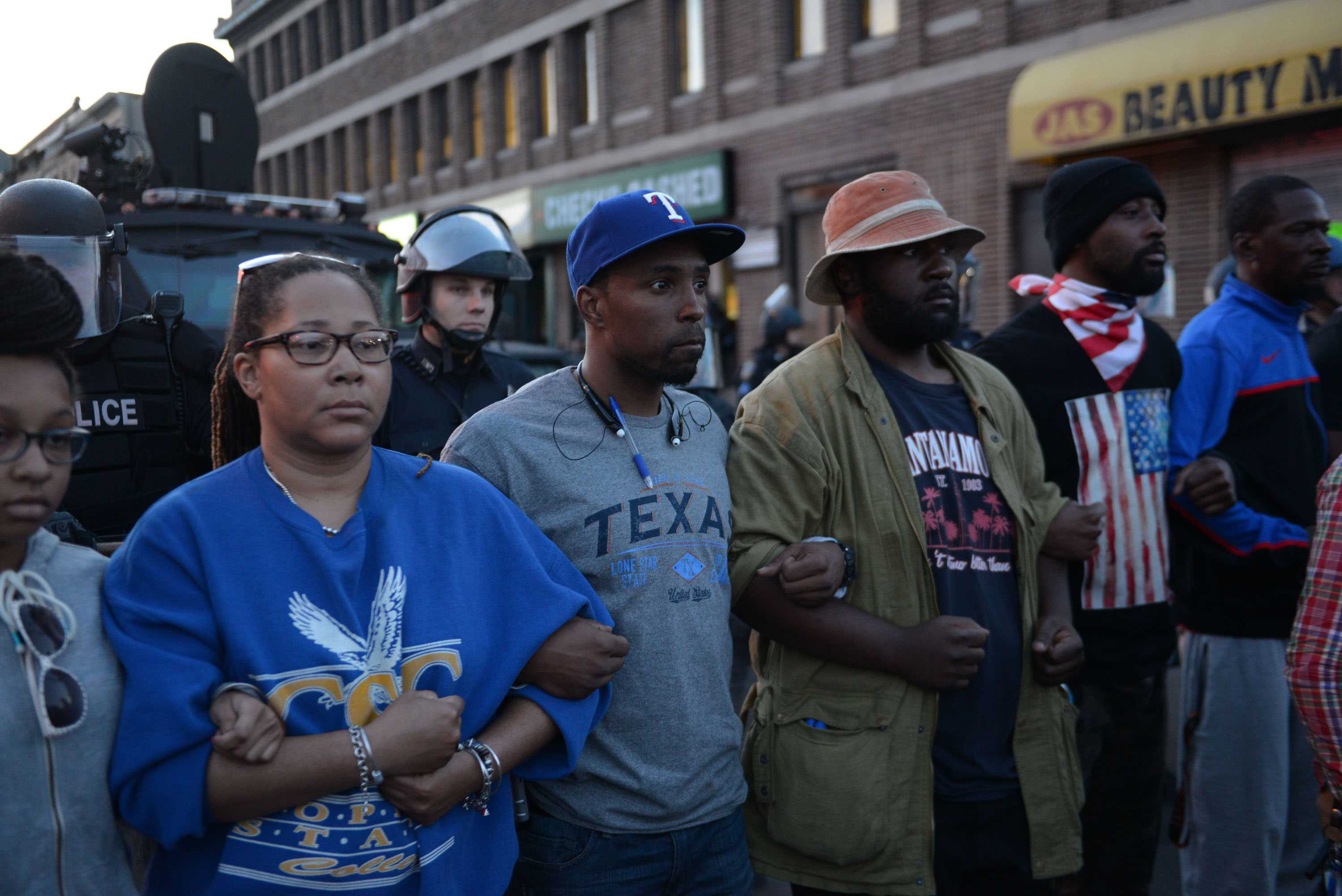 Peaceful Black protesters linking arms. Their expressions are stotic and strong.