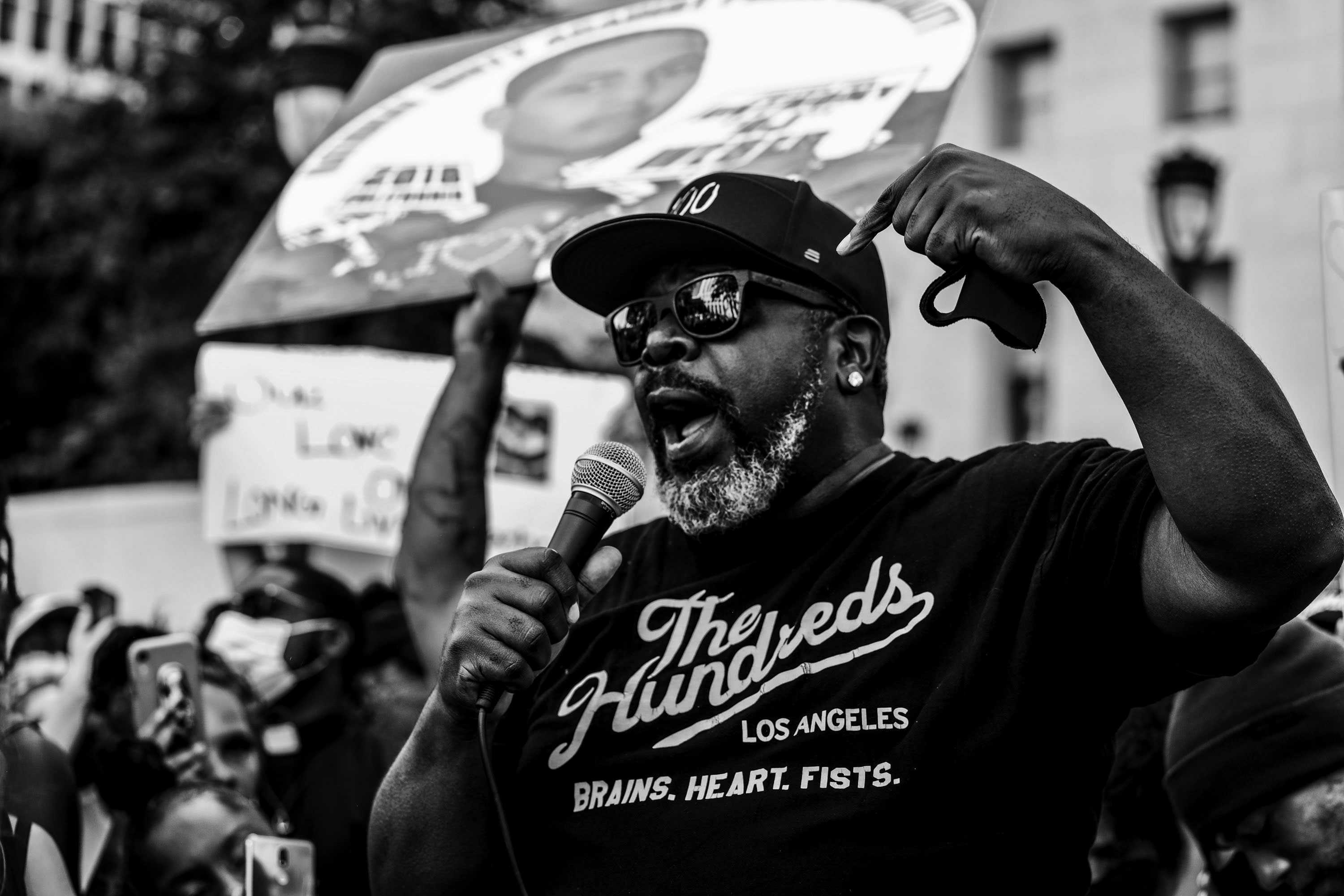 Cedric the Entertainer is right of center, addressing a crowd of protesters. He is shown from the chest up.