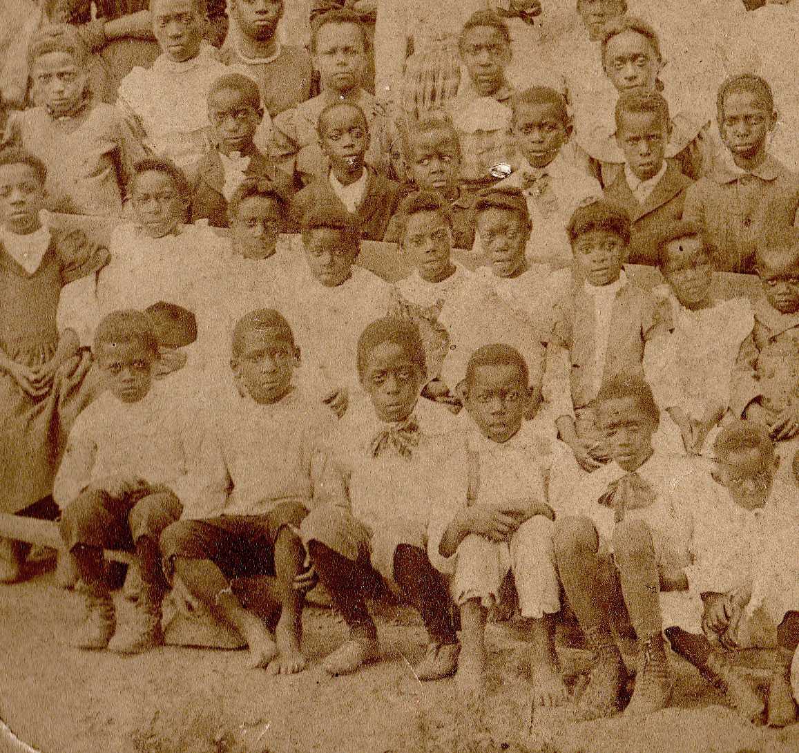 A sepia photograph of young students sitting together on benches for a school photograph.