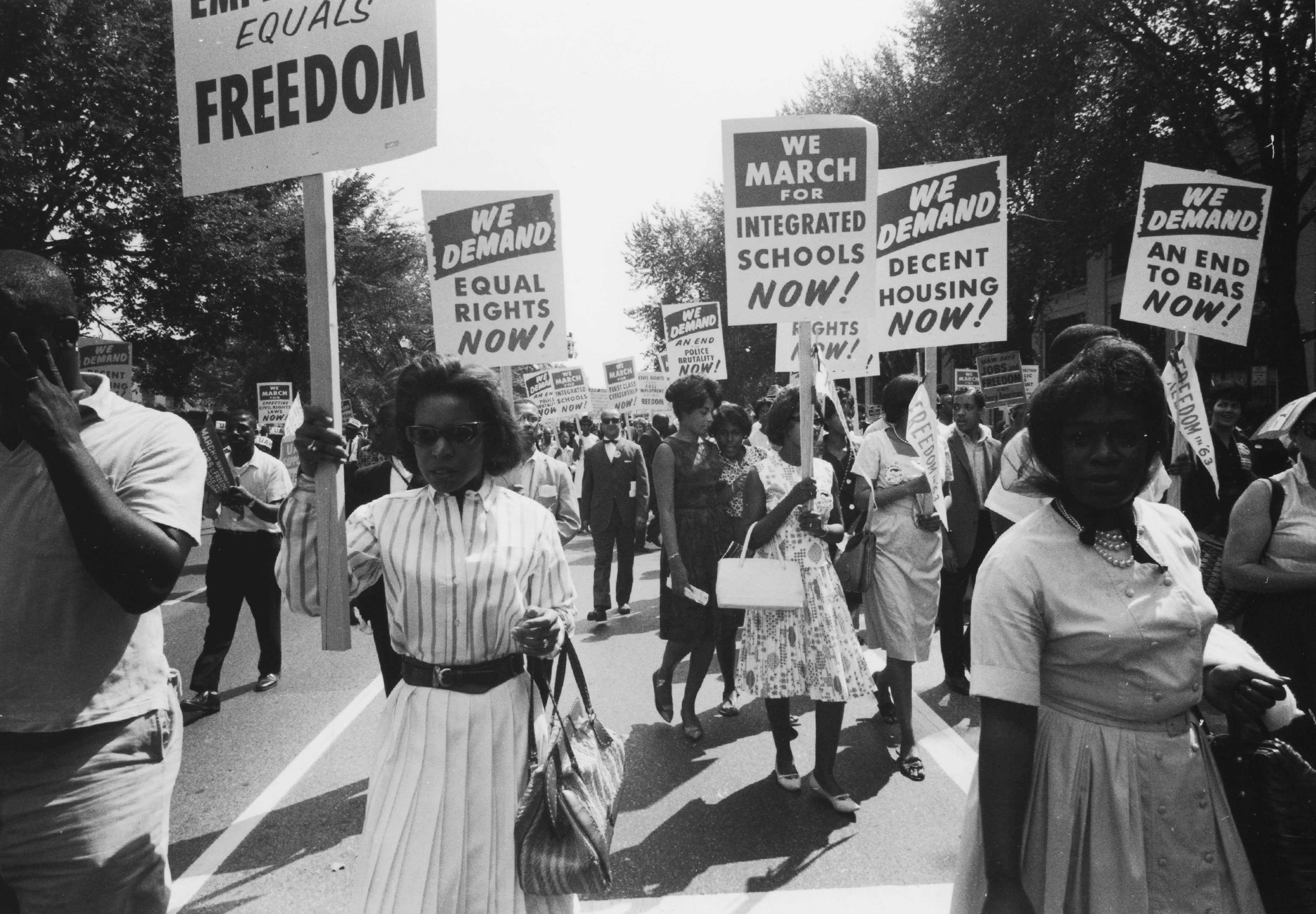 A black and white photograph of protesters walking with picket signs calling to intergrated schools.