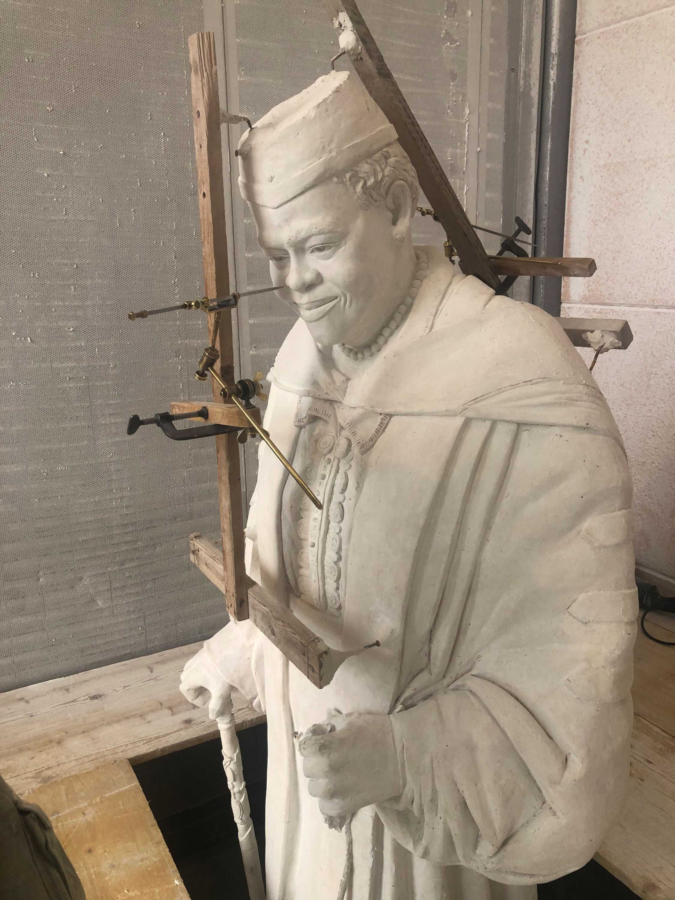 Color photograph of plaster sculpture being measured with various wooden instruments.