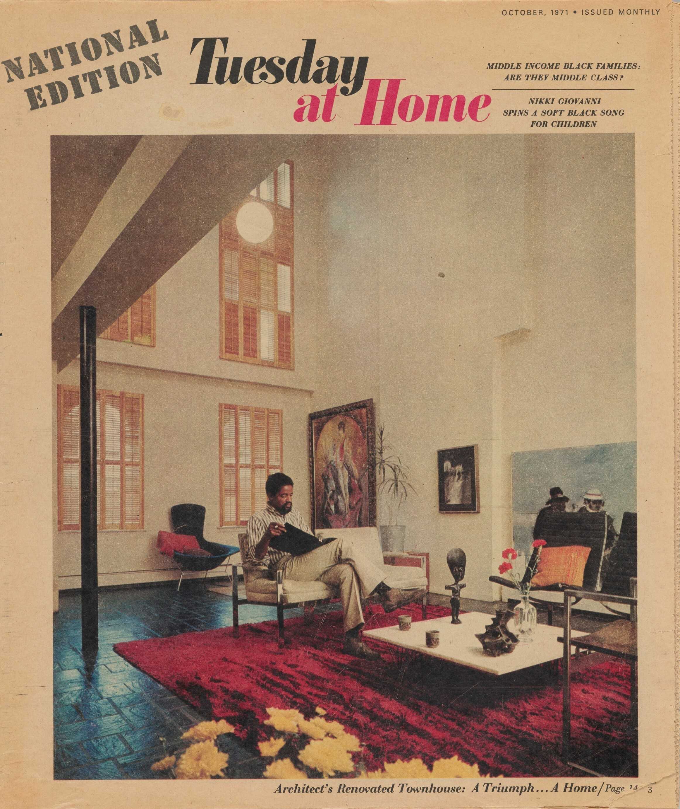 Magazine cover for "Tuesday at Home" showing man seated on a white couch in the center of the room. He is holding an open binder. The space has a red rug in the center over a stone floor with a few pieces of furniture in the room and artwork on the walls.