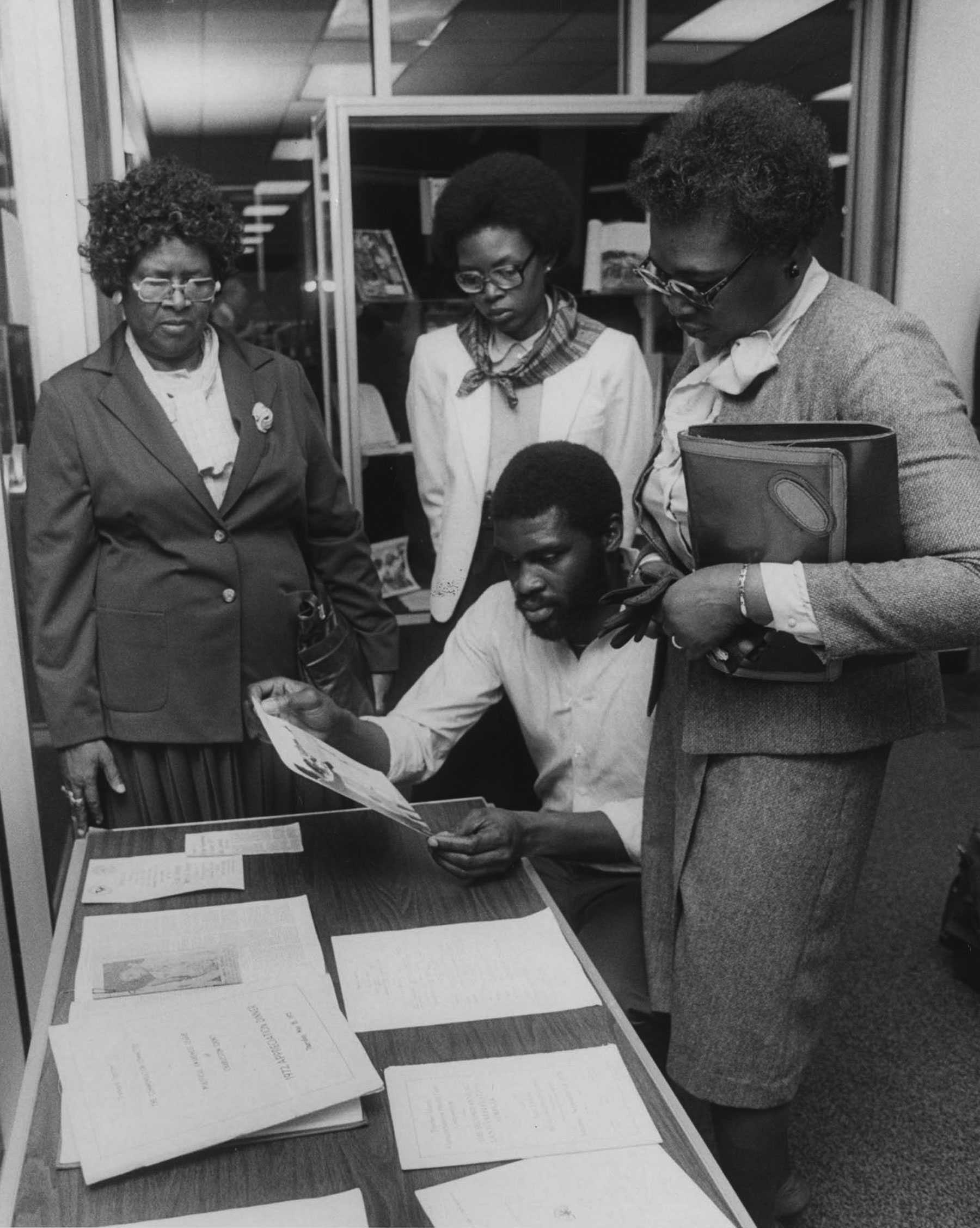 A black and white photo of the Jenkins Family looking at papers and a photos around a desk in the Esau Jenkins Exhibit