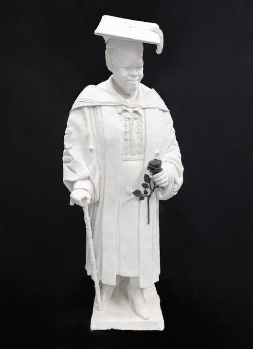 White plaster statue of woman dressed in academic regalia holding a black rose in her left hand and a walking cane in her right hand.