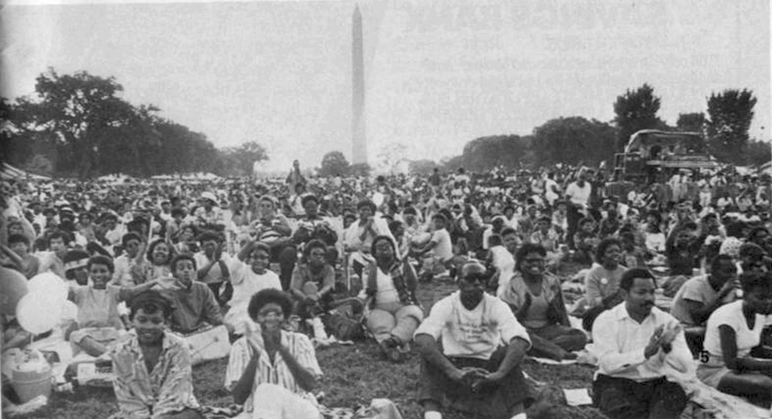 A older black and white photograph of many people sitting on the lawn in Washington, D.C.
