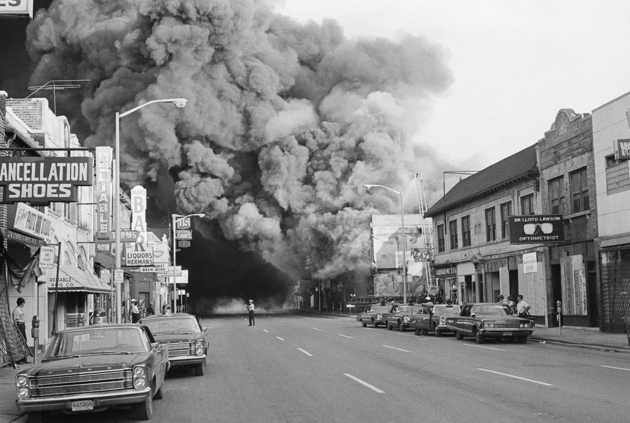 A black and white photograph of a large cloud expands and looms over a street on Detroit's West Side during racial riots.