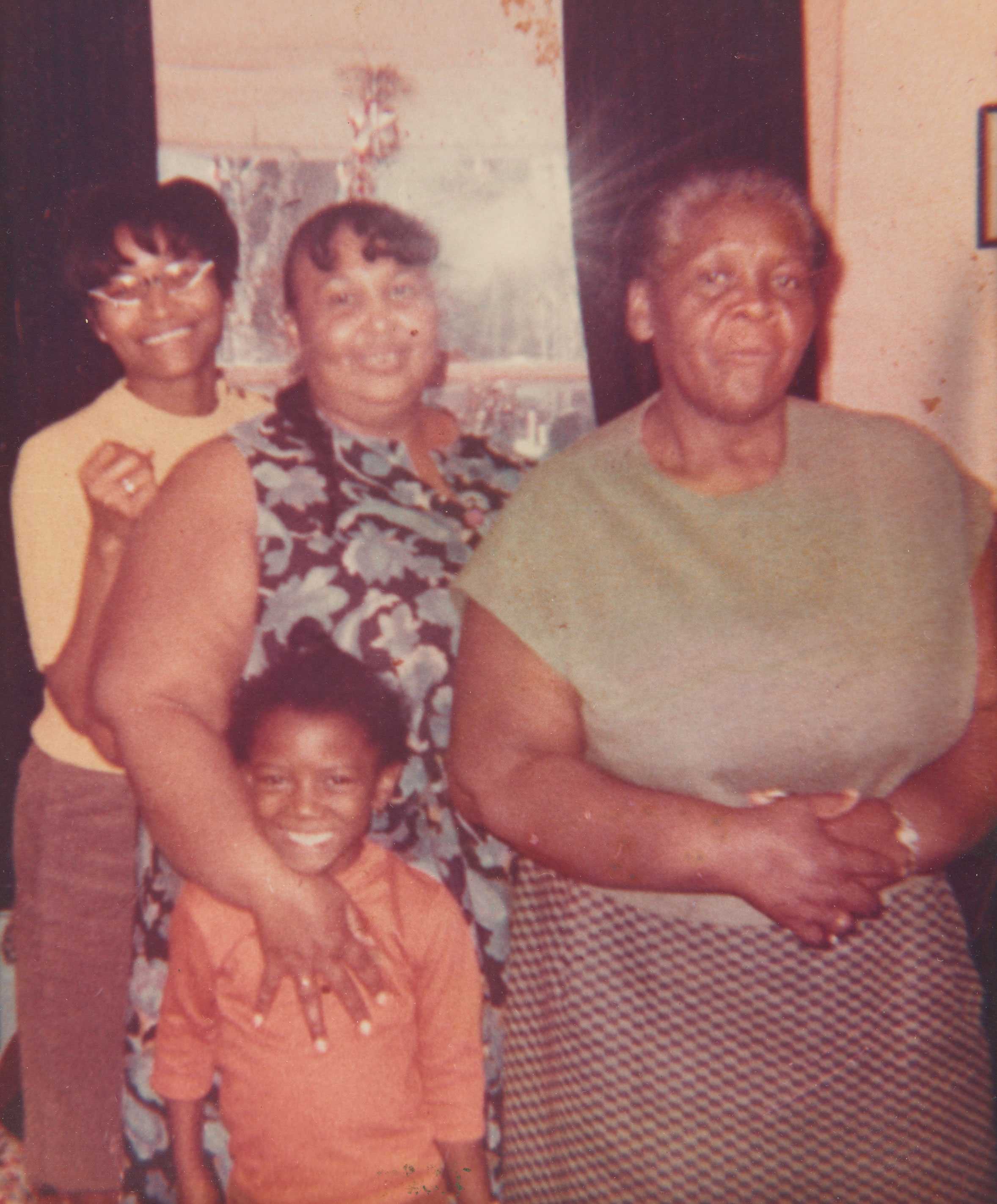 A color photograph of three women of different generations and a child standing together. The child is in front of the women.