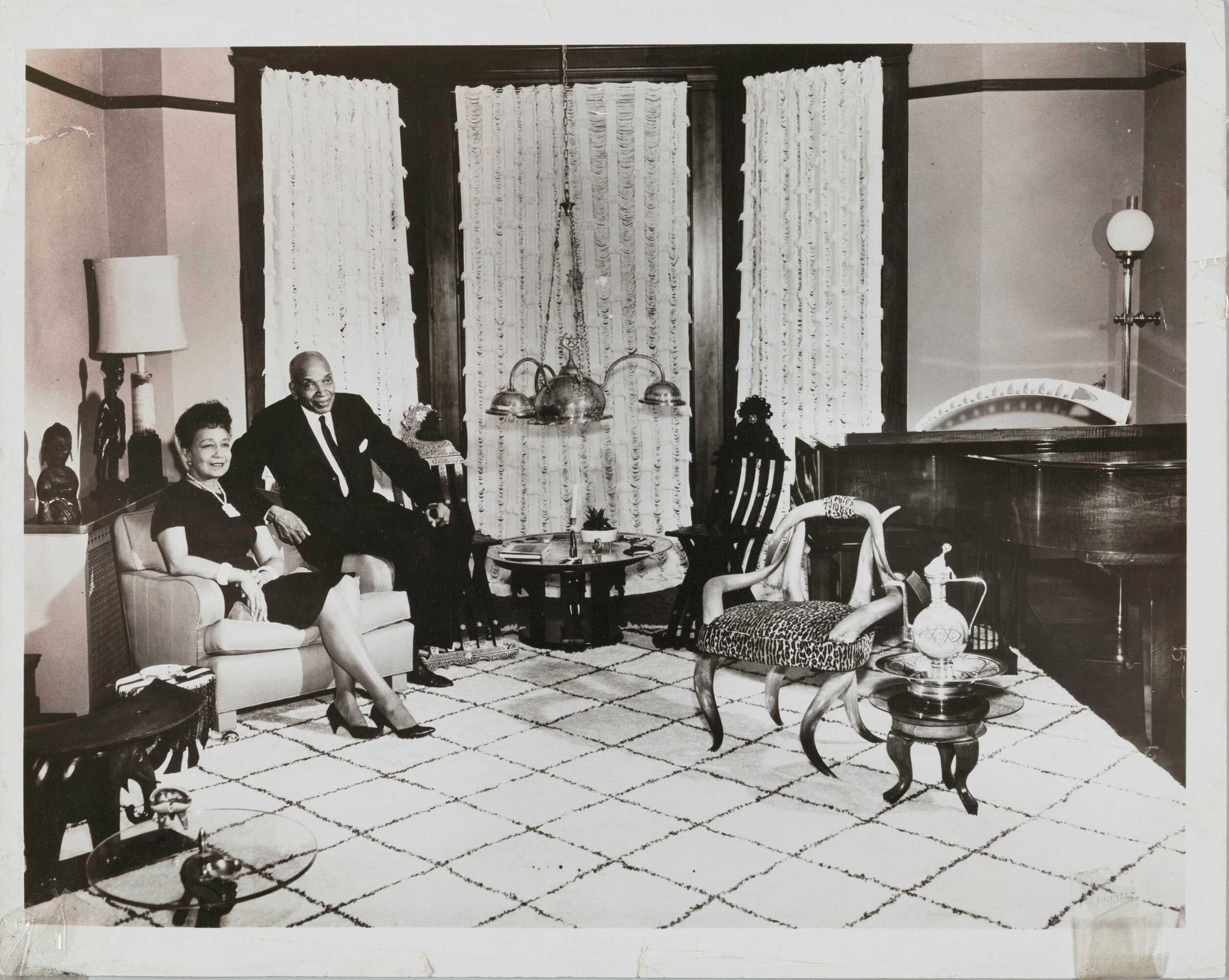 Black and white photograph of woman and a man seated next to each other in a highly decorated room.