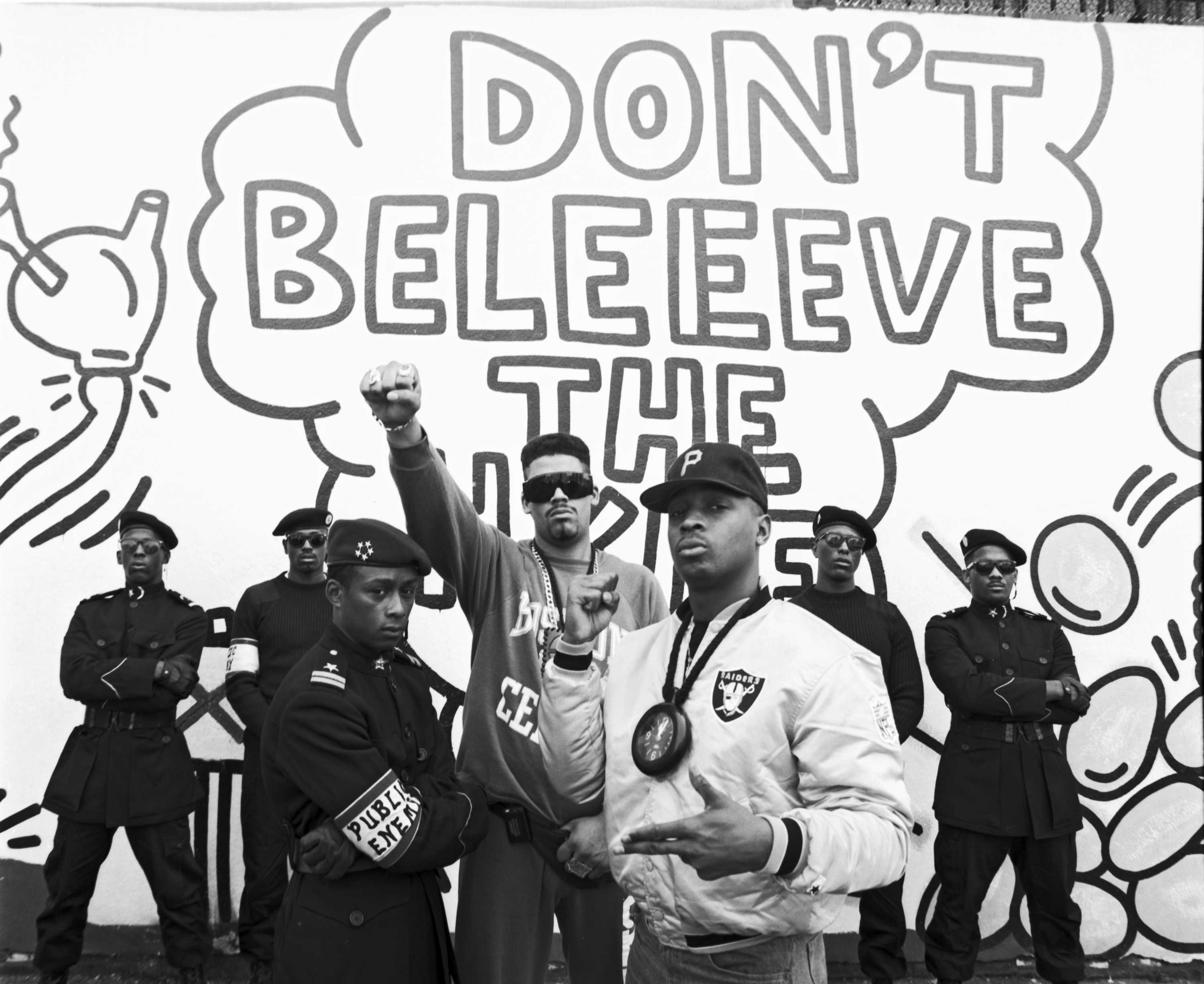 Public Enemy poses in front of a mural that says 'Don't Beleeve the...'