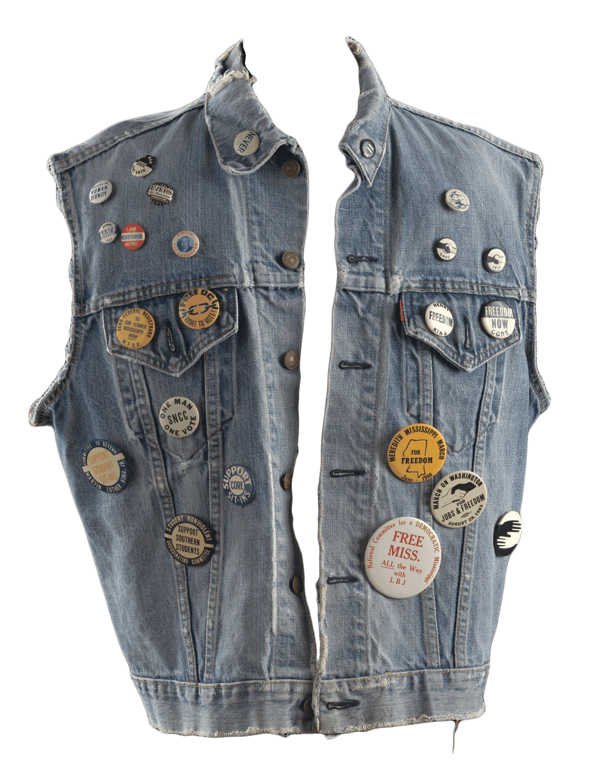 A light blue, worn denim vest with 23 pinback protest buttons pinned across the front.