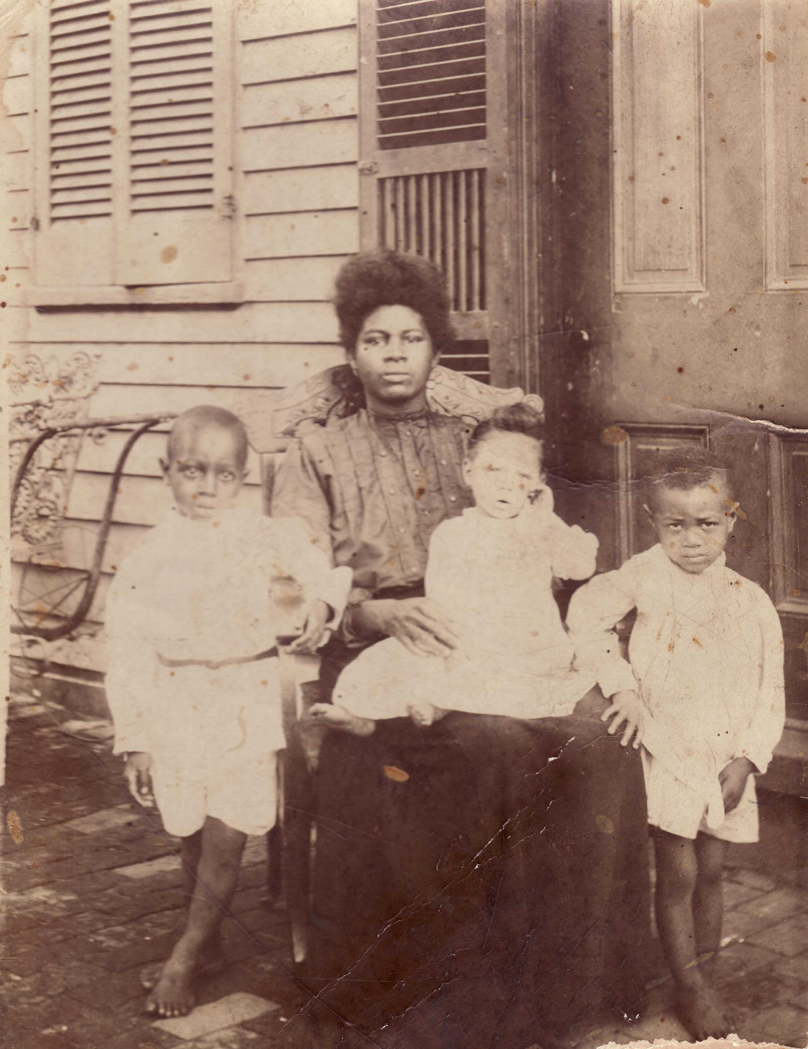 A worn old photograph of a mother sitting with a baby in her lap and two small children standing next to them.