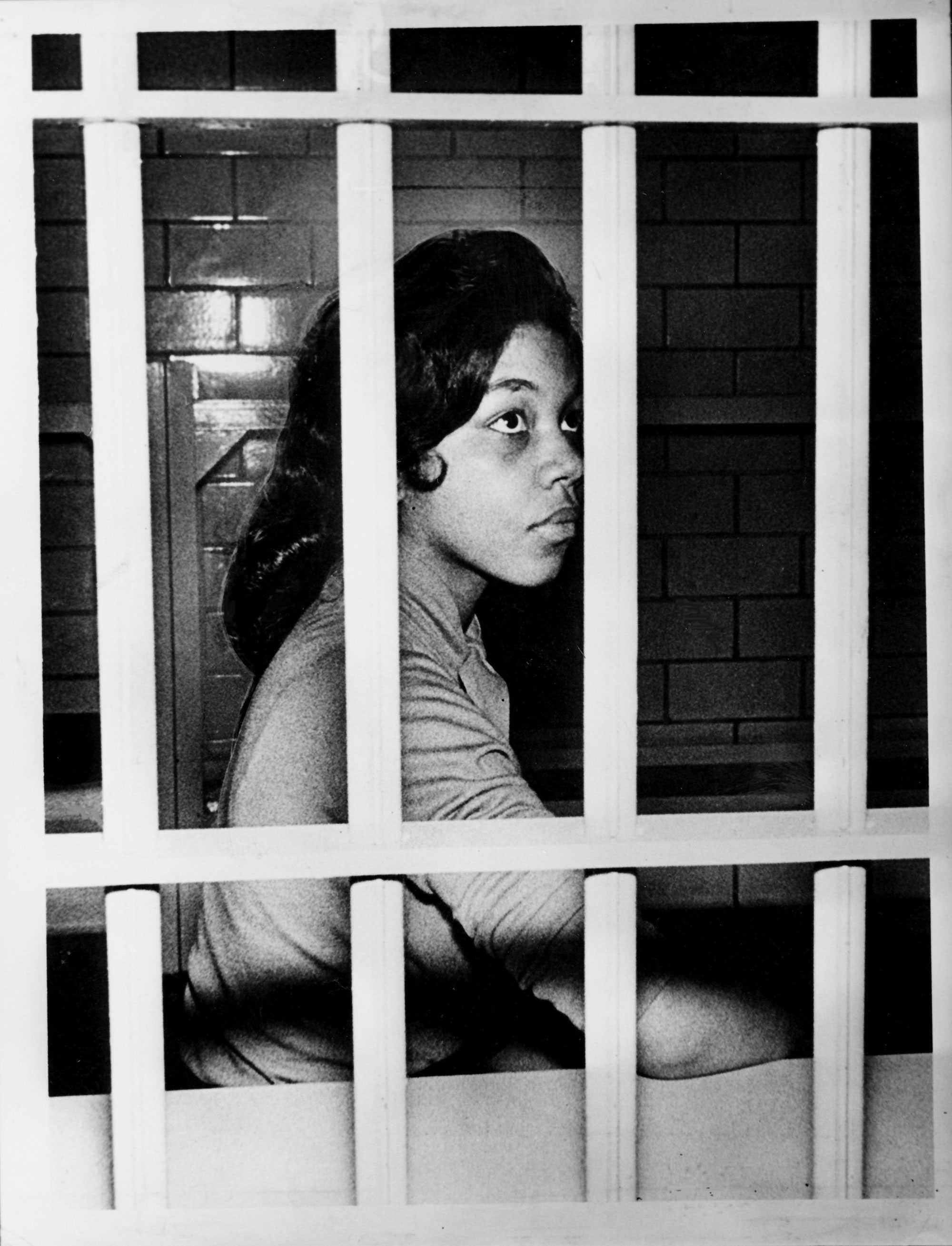 A protestor sits behind the prison bars. She is looking up with determined expression.