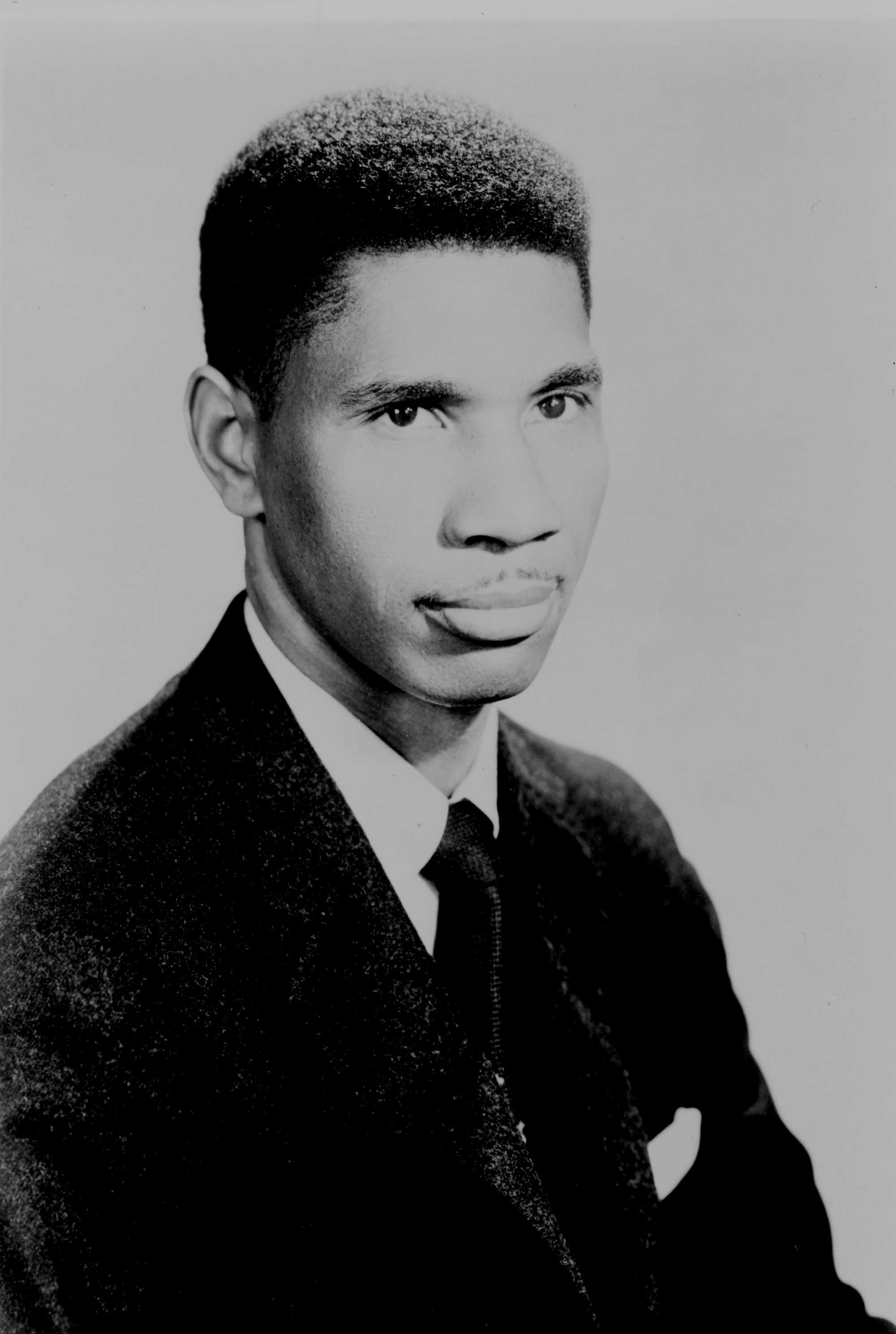 A black and white portrait of young Medgar Evers. He has a small mustache and dressed in a dark suit.