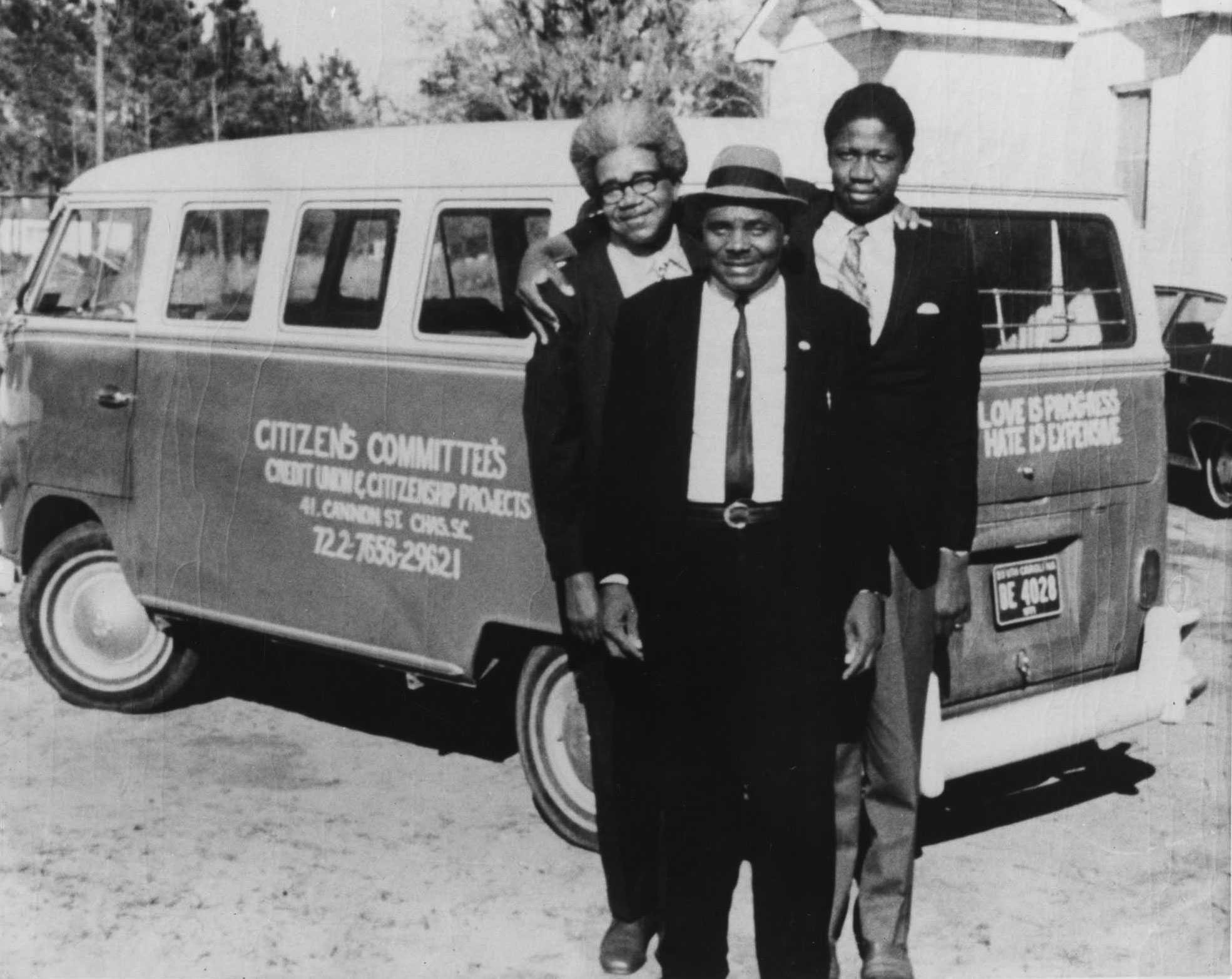 A black and white photograph of Esau Jenkins, Alfred Fields, and Rev. Willis Goodwin, holding each other outside of A Citizens Committee vban.