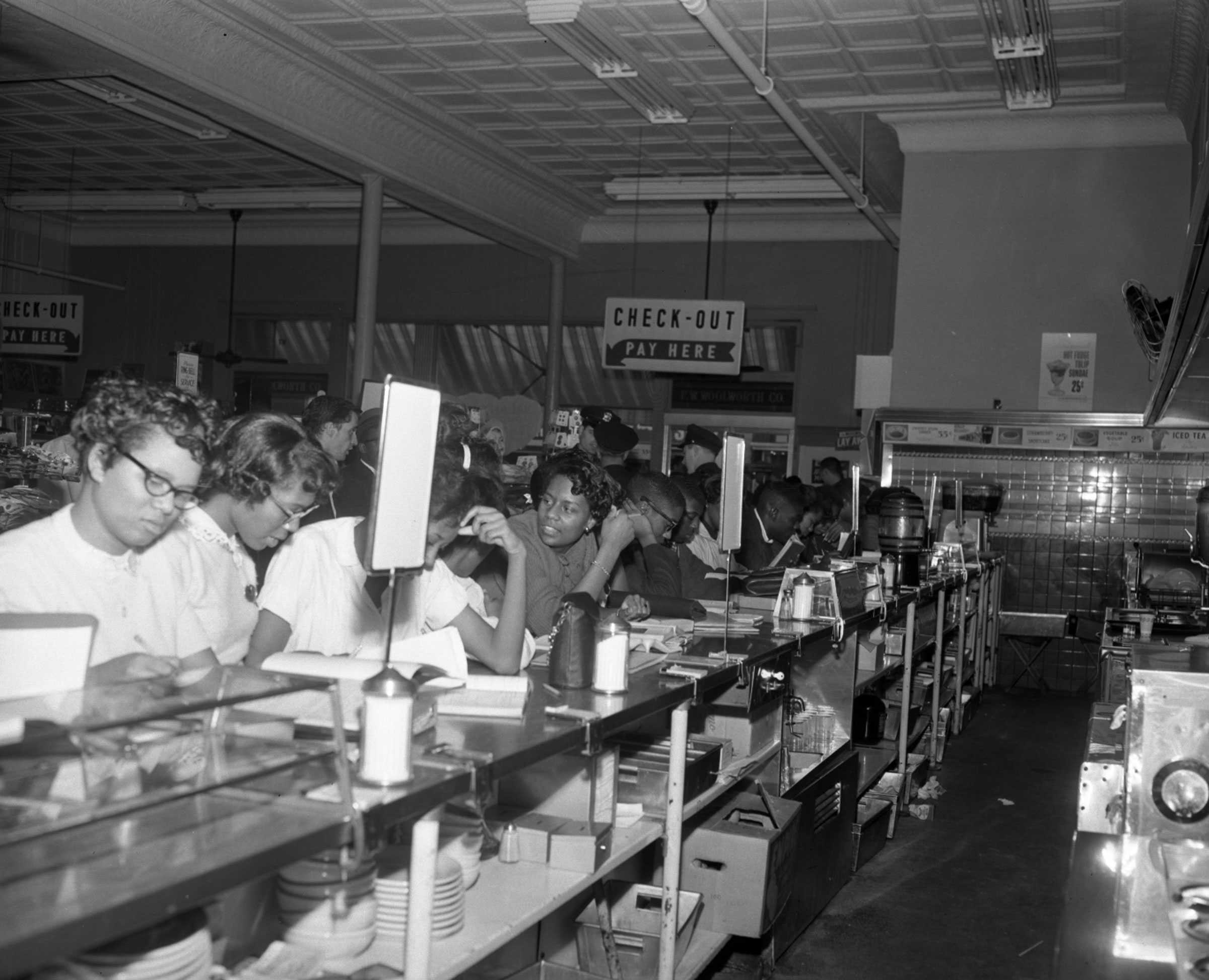 A black and white photograph of female students sitting at the Woolworth’s lunch counter in Greensboro.