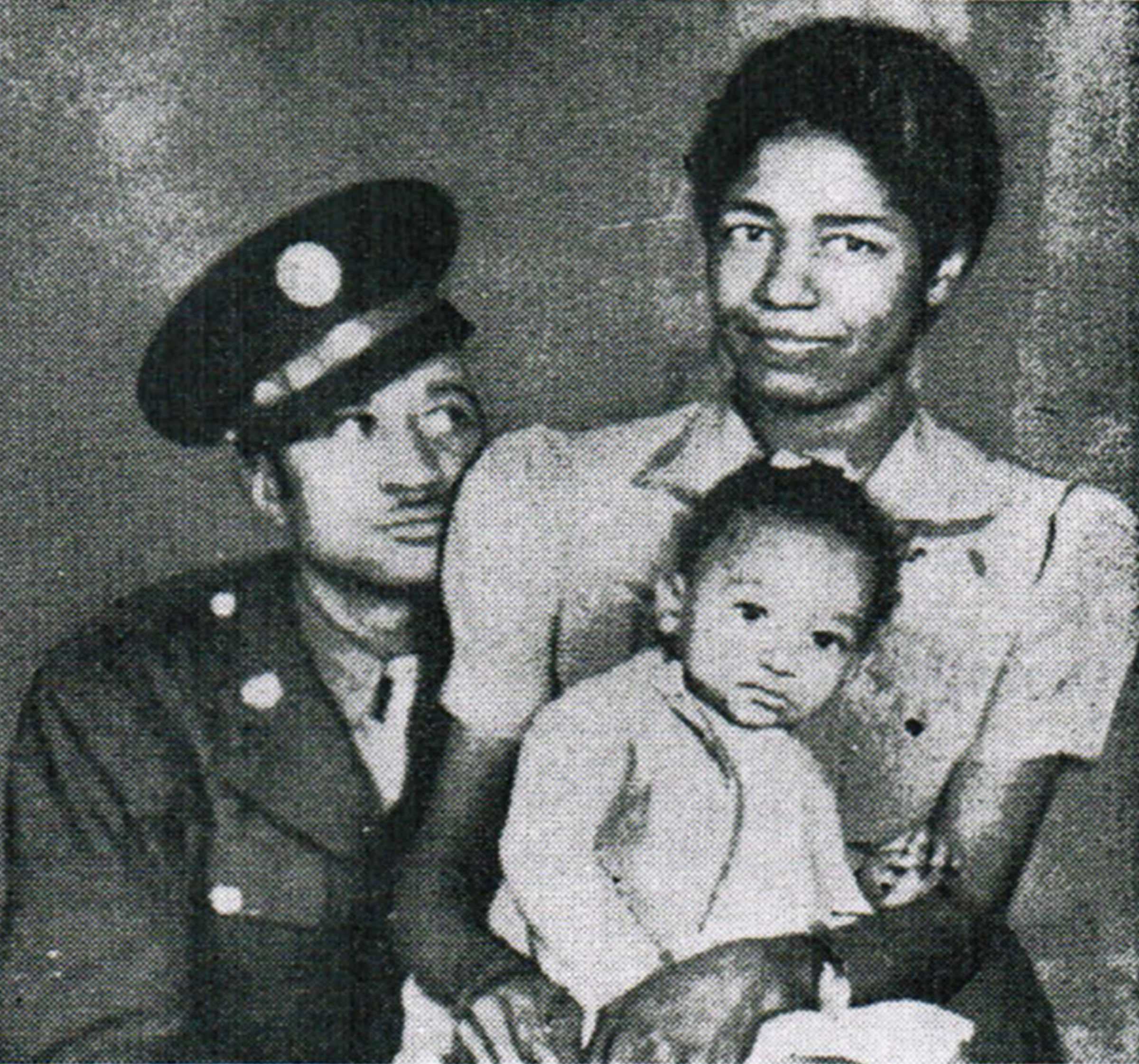 A blurry image of Cpl. John C. Jones with his wife and 4 years old daughter. He is dressed in his uniform, resting his head on his wife's shoulder.