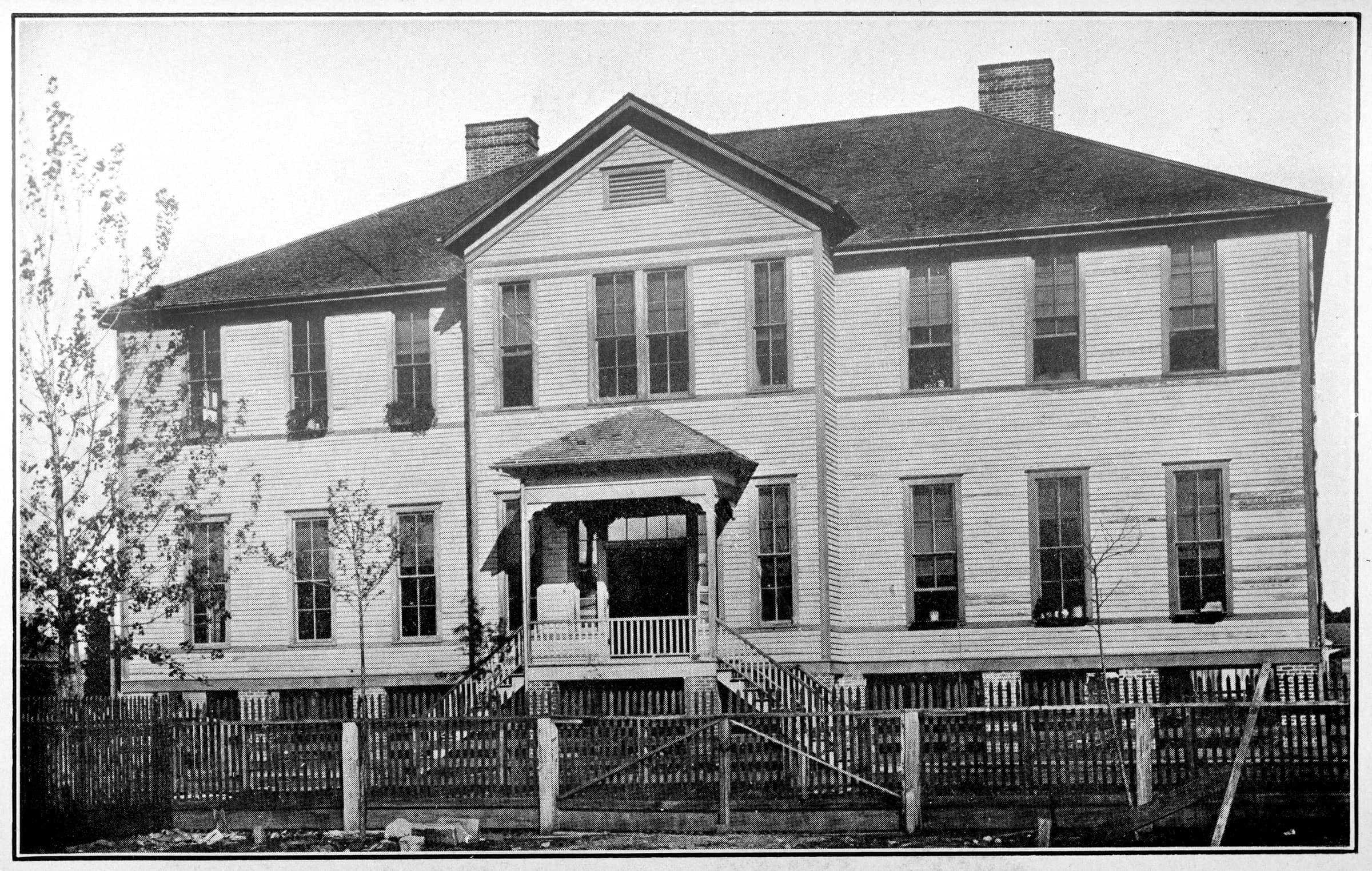 A black and white photography of outside of the Gregory School. Its a two story school with white siding.