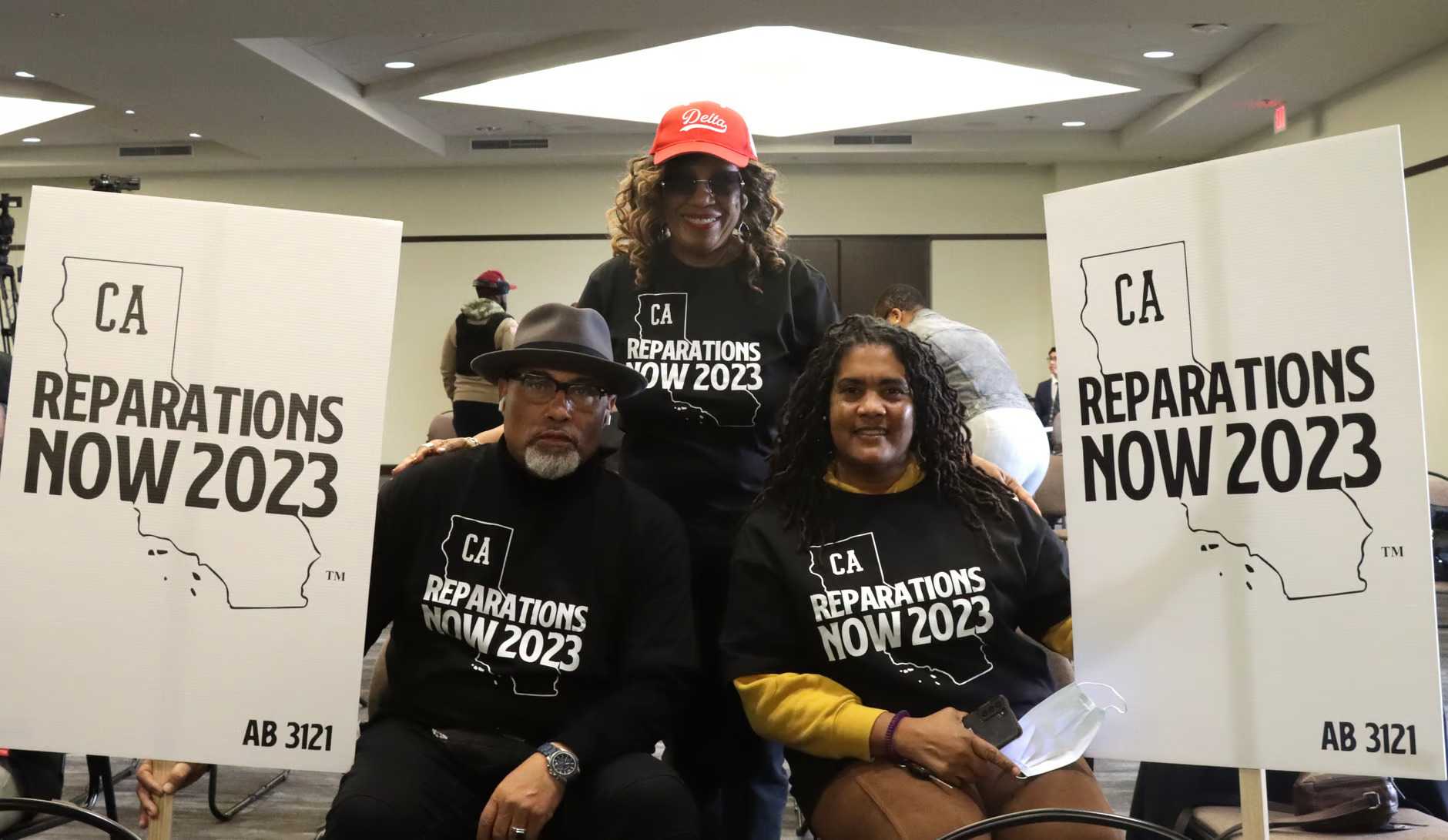 Three protestors pose for the a picture with their CA Reparations Now 2023 signs, shirts, and hat.