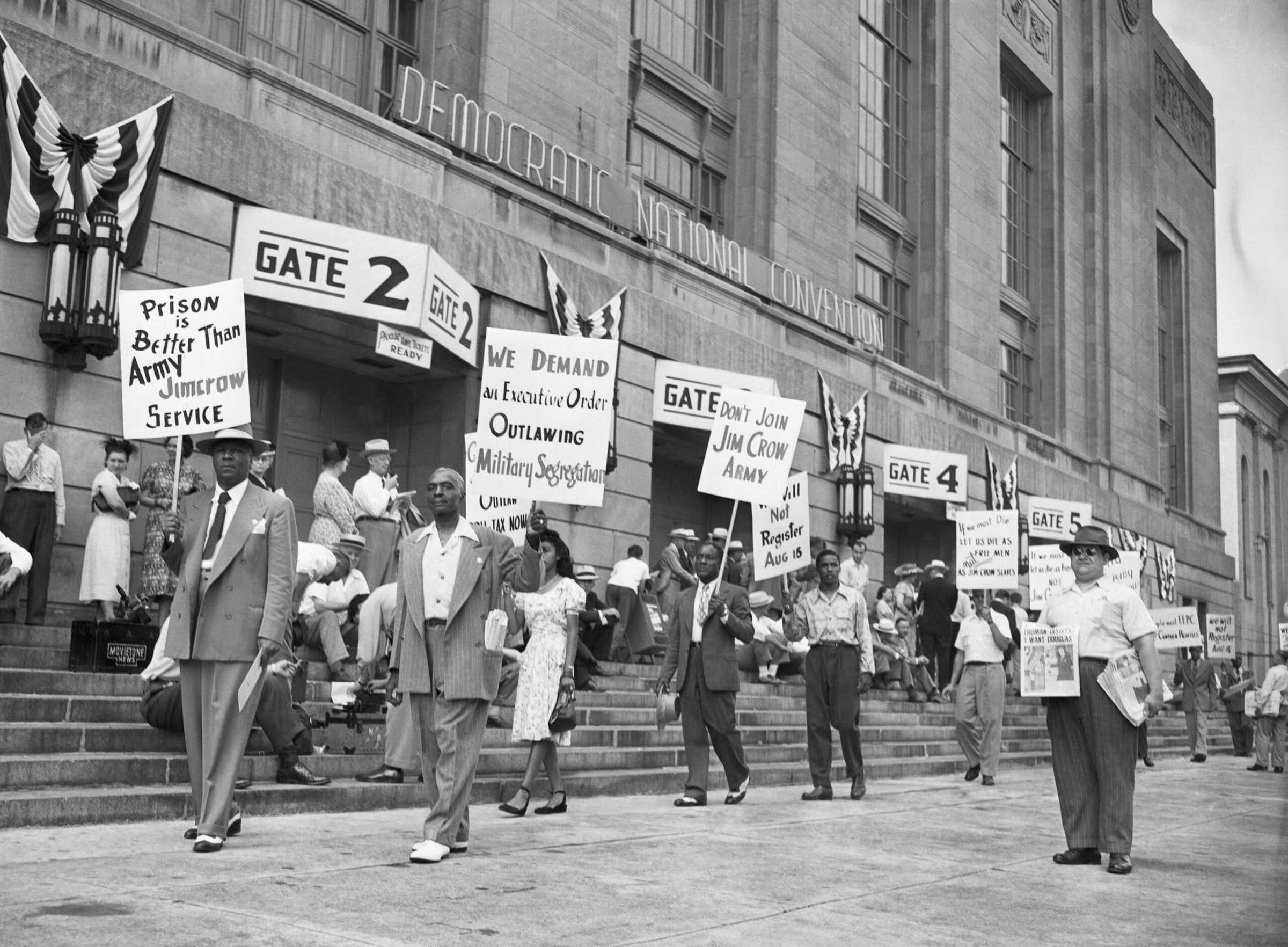 Black and white photograph showing people protesting outside building identified as the "DEMOCRATIC NATIONAL CONVENTION" building.  Protesters are carrying signs saying "We Demand an Executive Order Outlawing Military Segregation" and "Prison is Better Than Army Jimcrow Service."