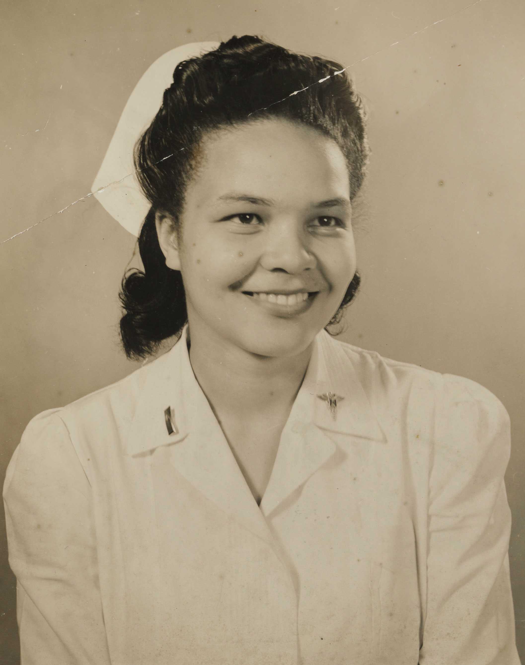 A sepia-toned photo of Lt. Louise Lomax in a white nurse's uniform and cap, smiling and looking forward.