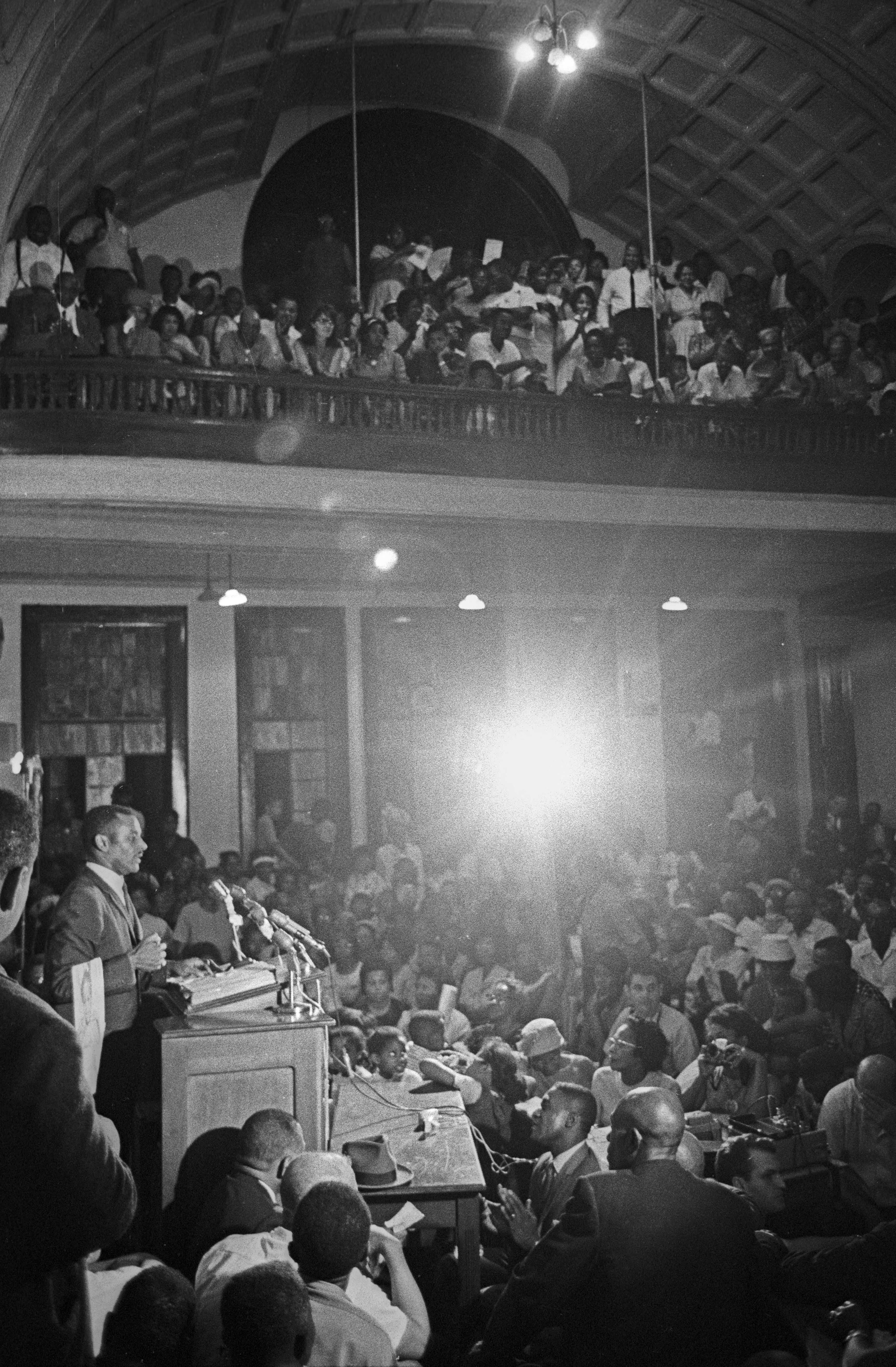 Black and white photograph of man at podium speaking to a large audience.