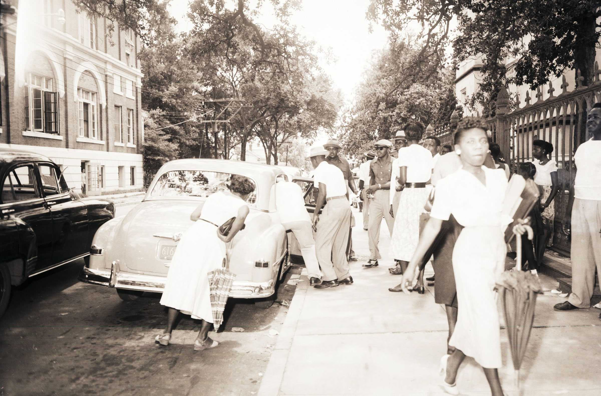 A black and white photograph of boycotters, men and women, gathering to get into a carpool outside the Old State Capitol building.