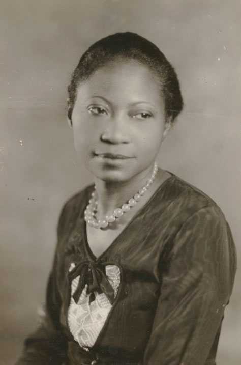 Half-length portrait of young Black woman wearing a dark dress with white lace details and a strand of pearls.