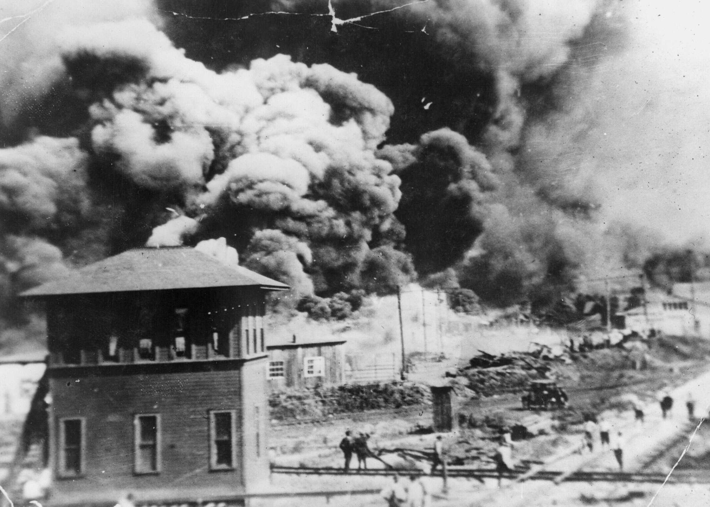 A black and white photograph of the buildings on fire in Tulsa with large clouds of smoke.