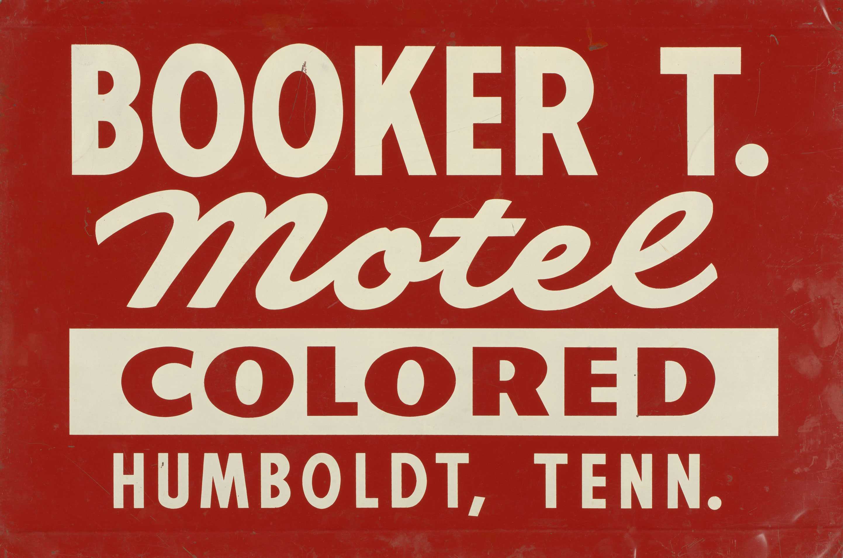 A red and white painted metal motel sign inside a plain wooden frame. The sign reads "Booker T. Motel COLORED Humboldt, Tenn."