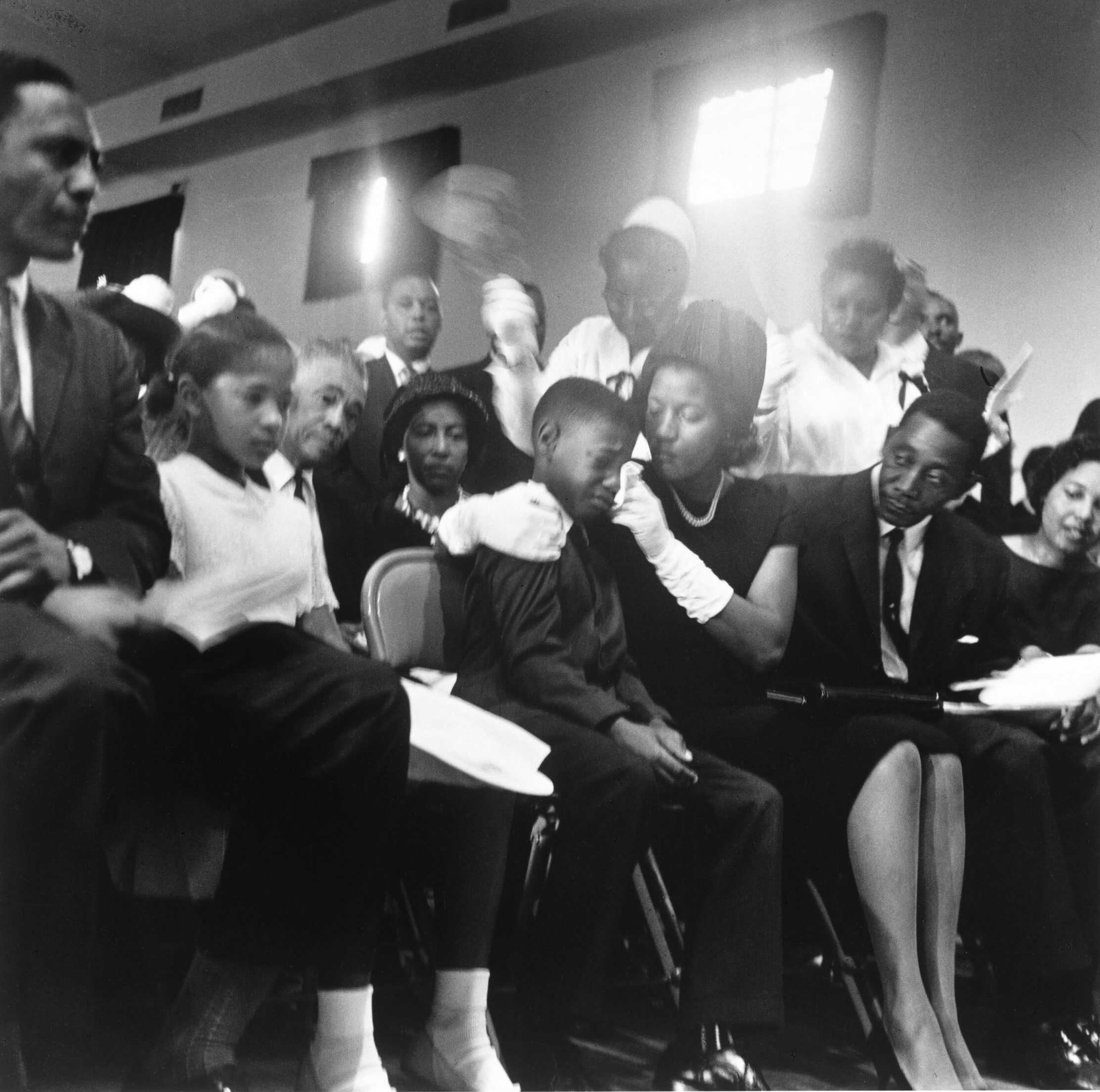 Black and white photograph showing Myrlie Evers comforting her children during services for their father.