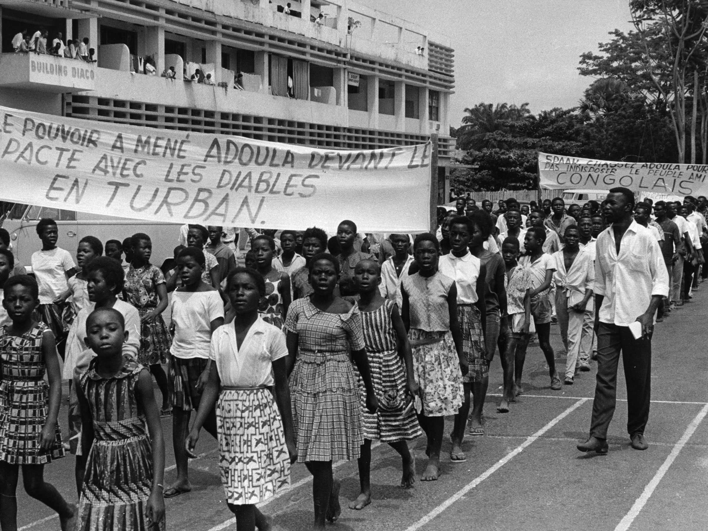 Children protesting as they walk in parallel lines holding large protest banner.