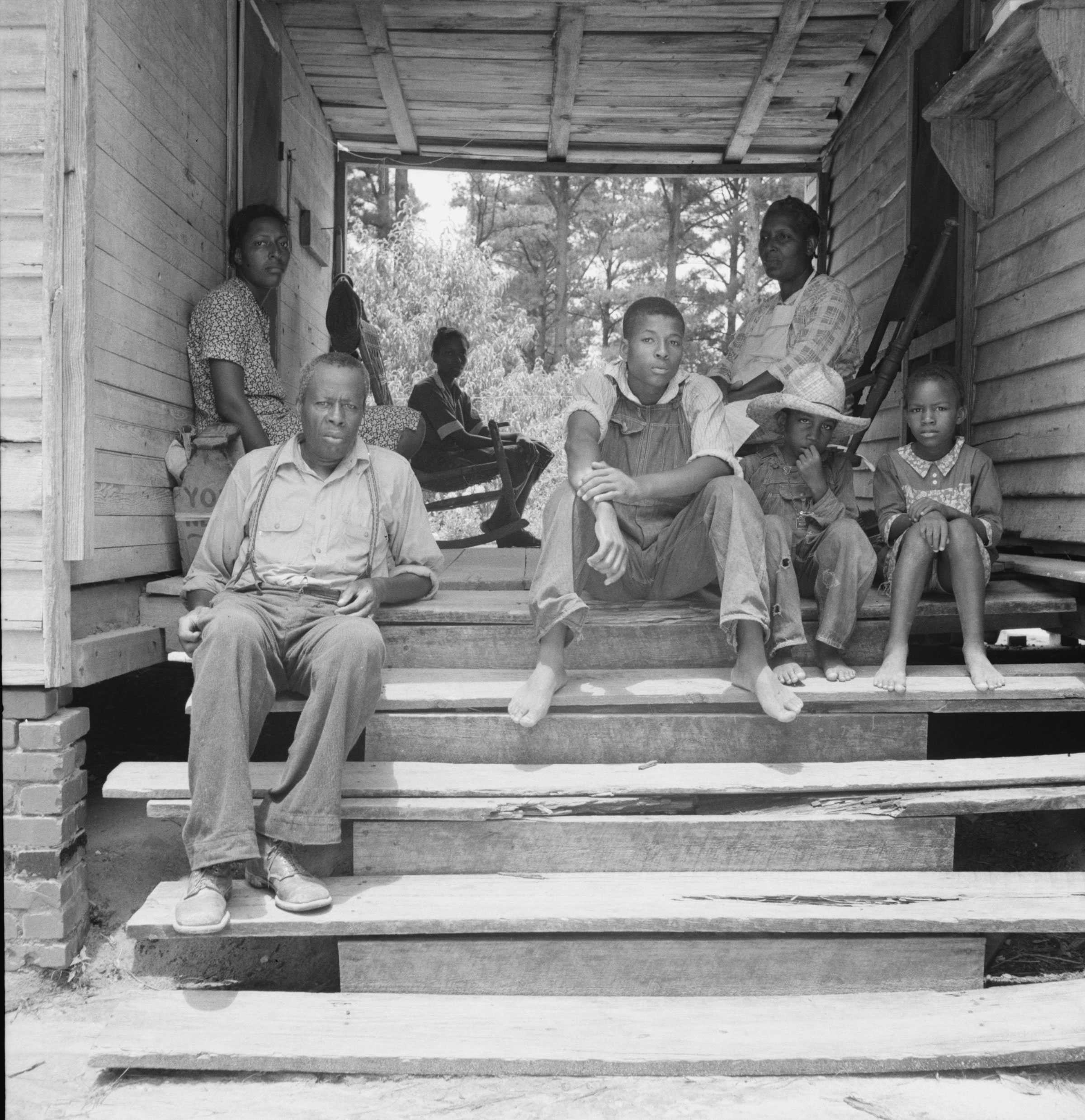 Black and white photograph of African American family seated on a porch of their home.