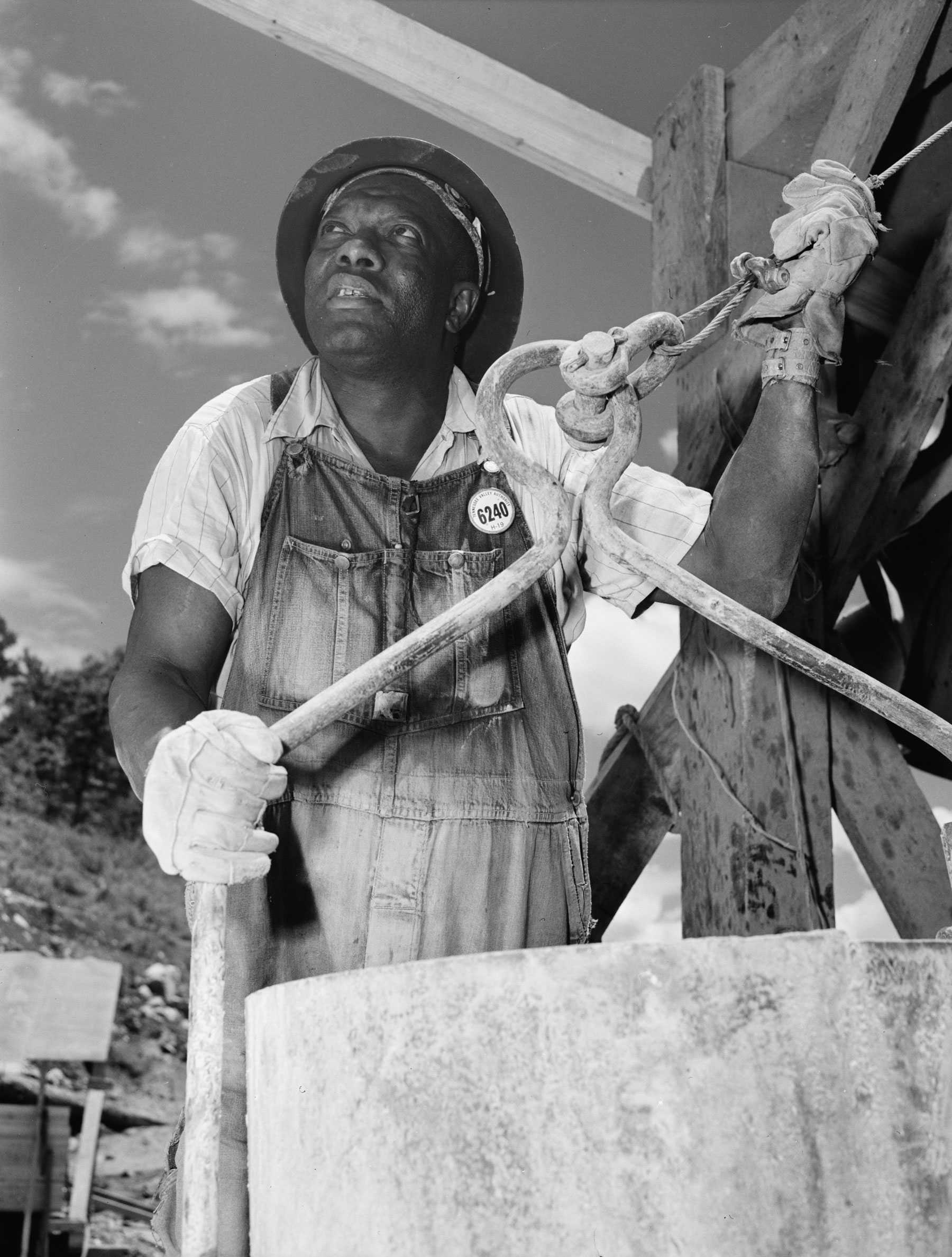 Black and white photograph of an African American man working at a well.  He is dressed in hard hat and overalls.