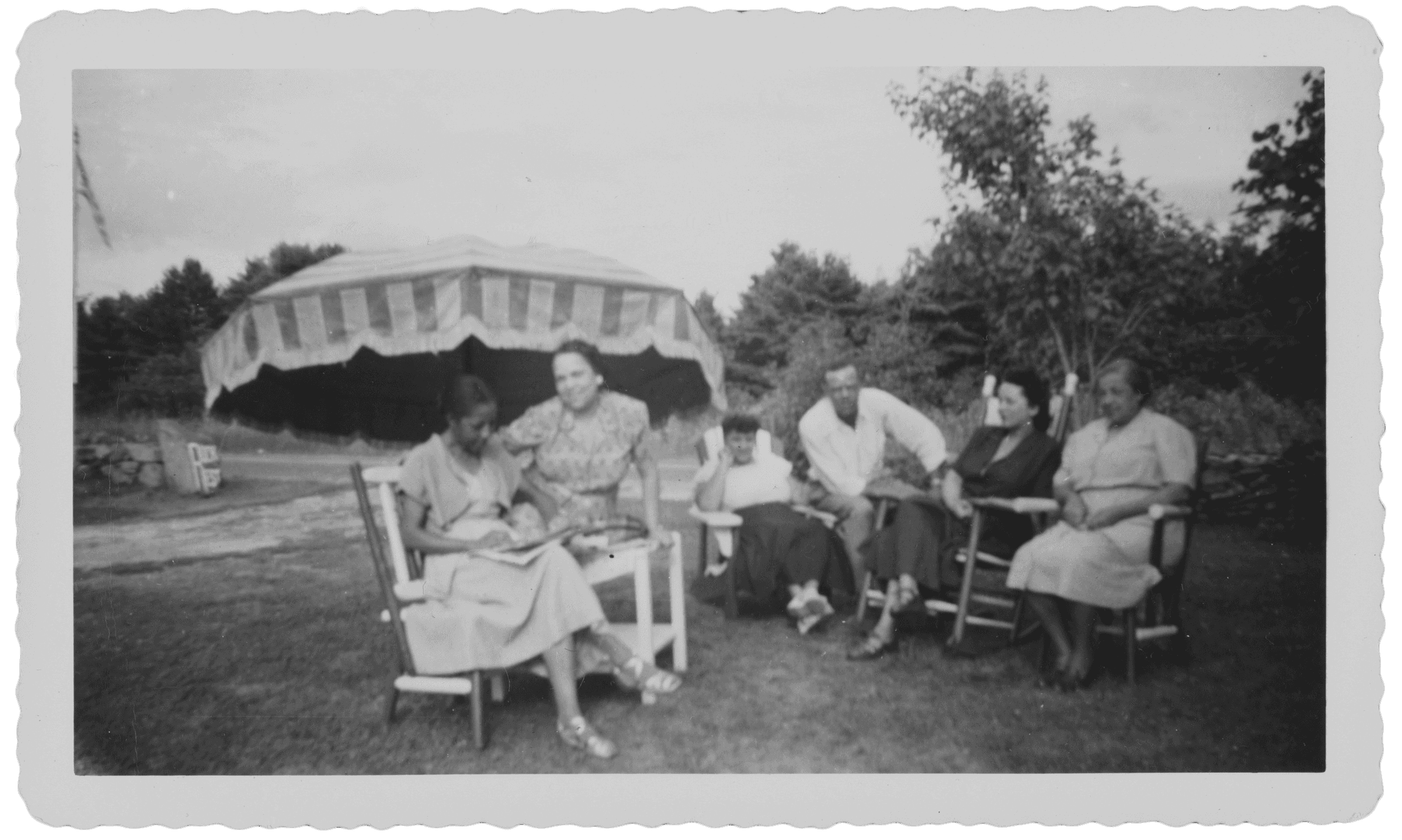 A black-and-white photograph of six people socializing on the lawn of the Rock Rest Tourist Home. Five women and one man are seated in chairs arranged in a semi-circle.